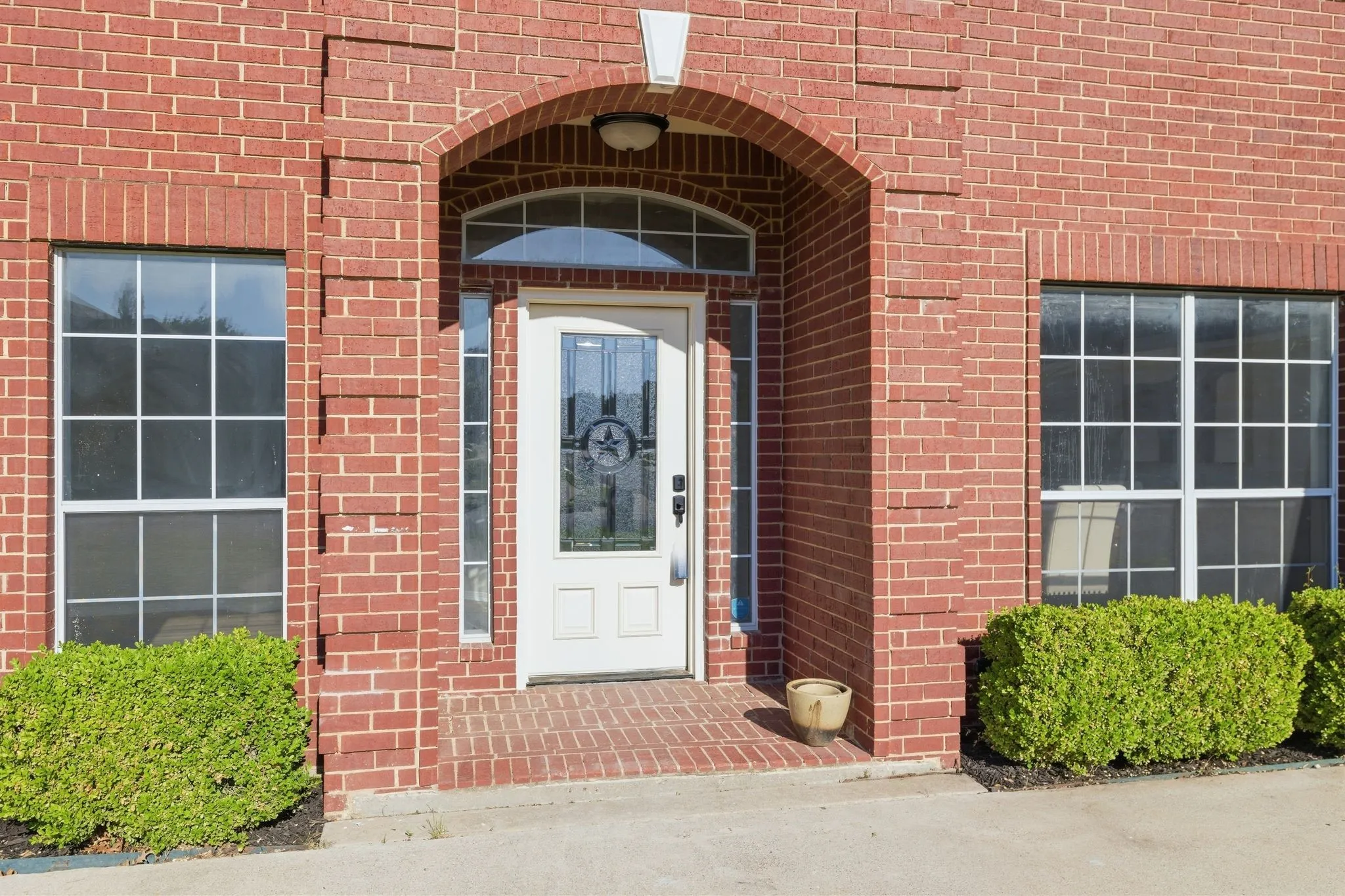 Brick exterior featuring an arched entry, transom window, sidelights, and grid-pattern windows