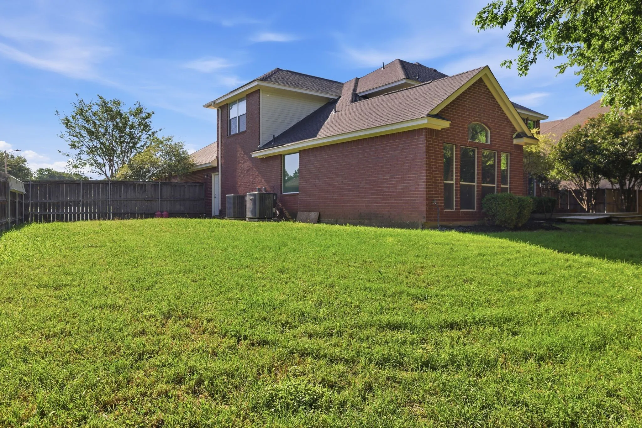 Spacious green lawn with a brown brick exterior and dark roof shingles