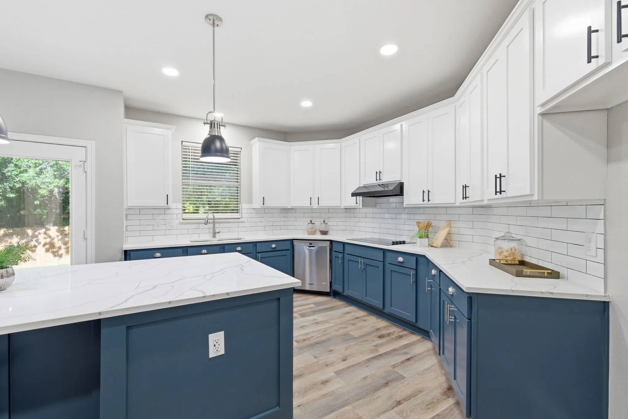 Modern kitchen featuring a large central island with a quartz countertop, two-tone cabinetry, stainless steel appliances, white subway tile backsplash, and wood-finish flooring