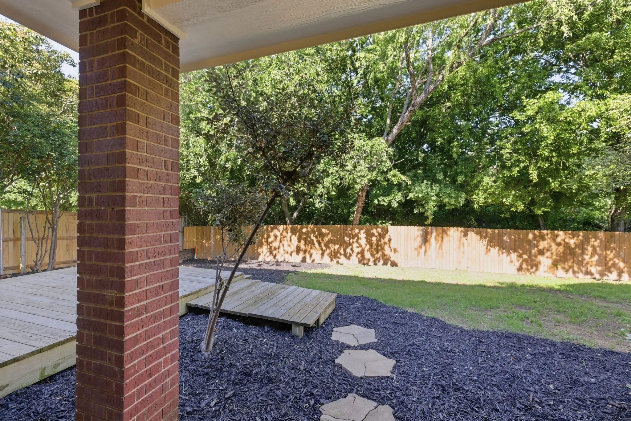 Covered patio with a brick column, wood decking, and a wood privacy fence