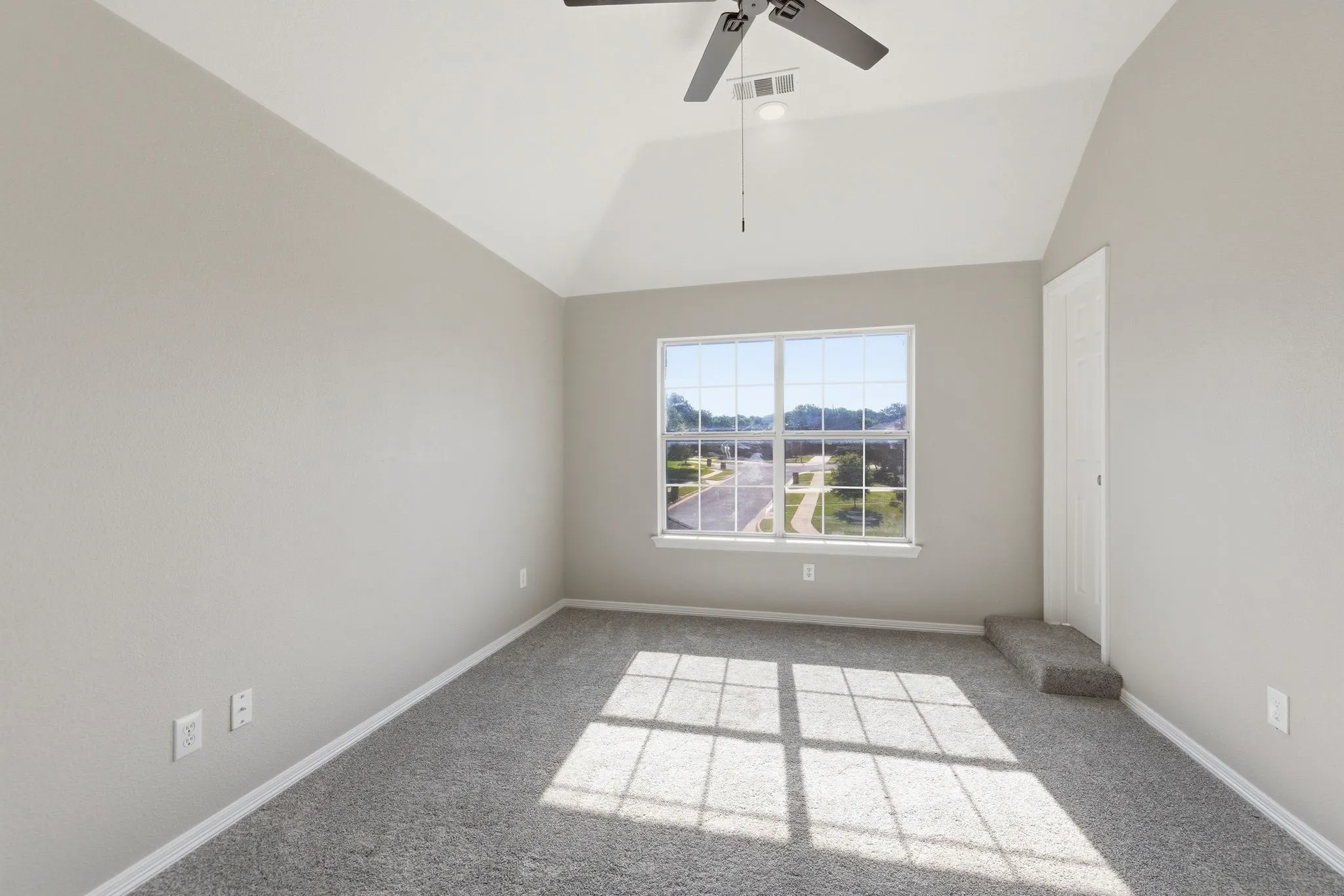 Vaulted ceiling room featuring light gray carpeting and a large window