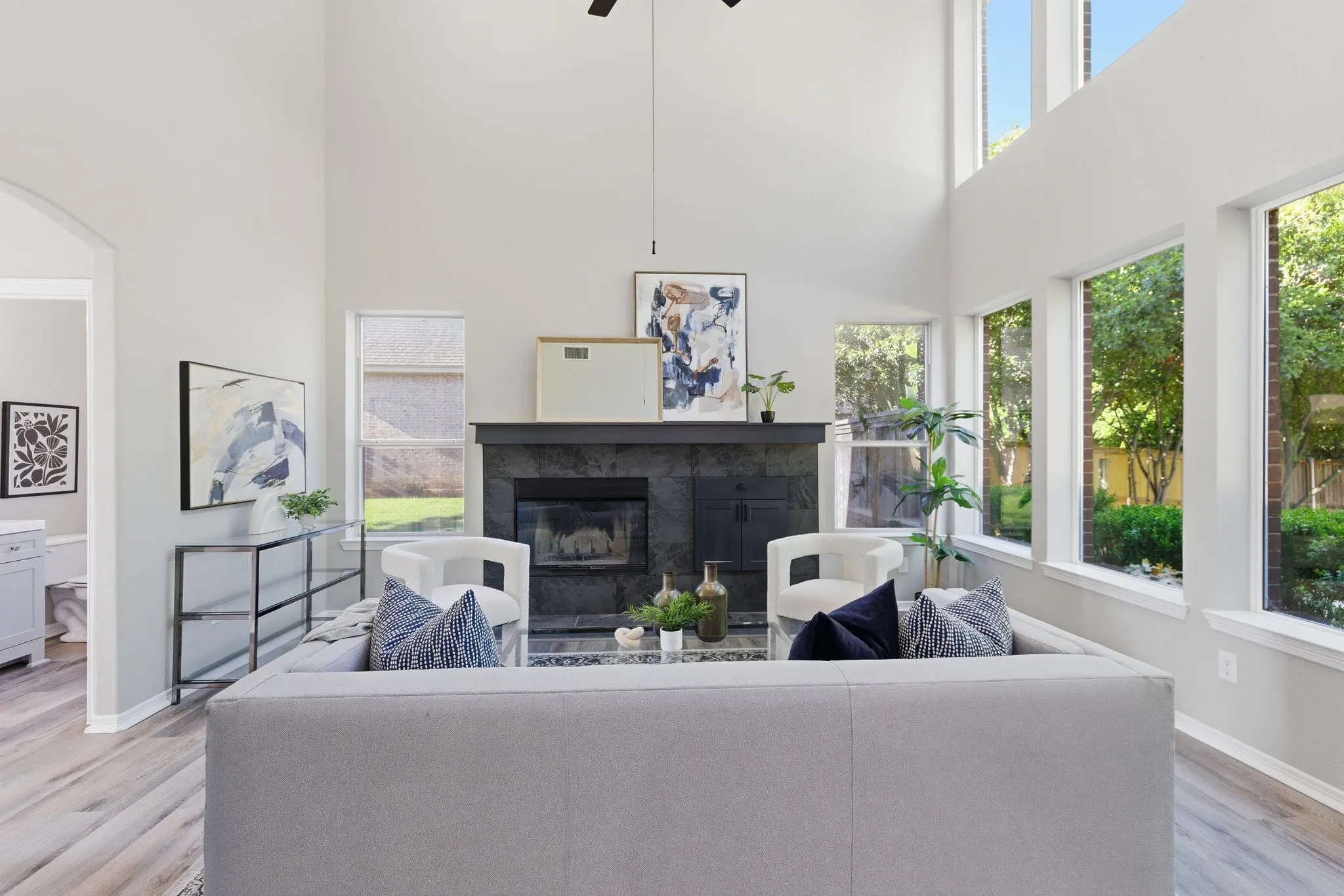 Spacious living area featuring a two-story ceiling, a black slate fireplace, wood-finish flooring, and multiple large windows