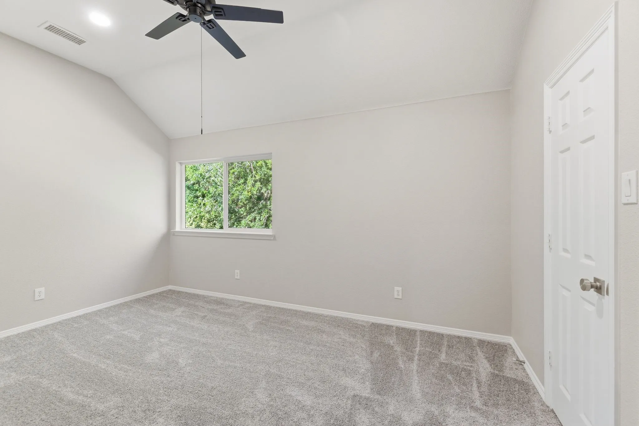 Carpeted room featuring a vaulted ceiling with a ceiling fan, recessed lighting, a window with exterior foliage, and a white paneled door