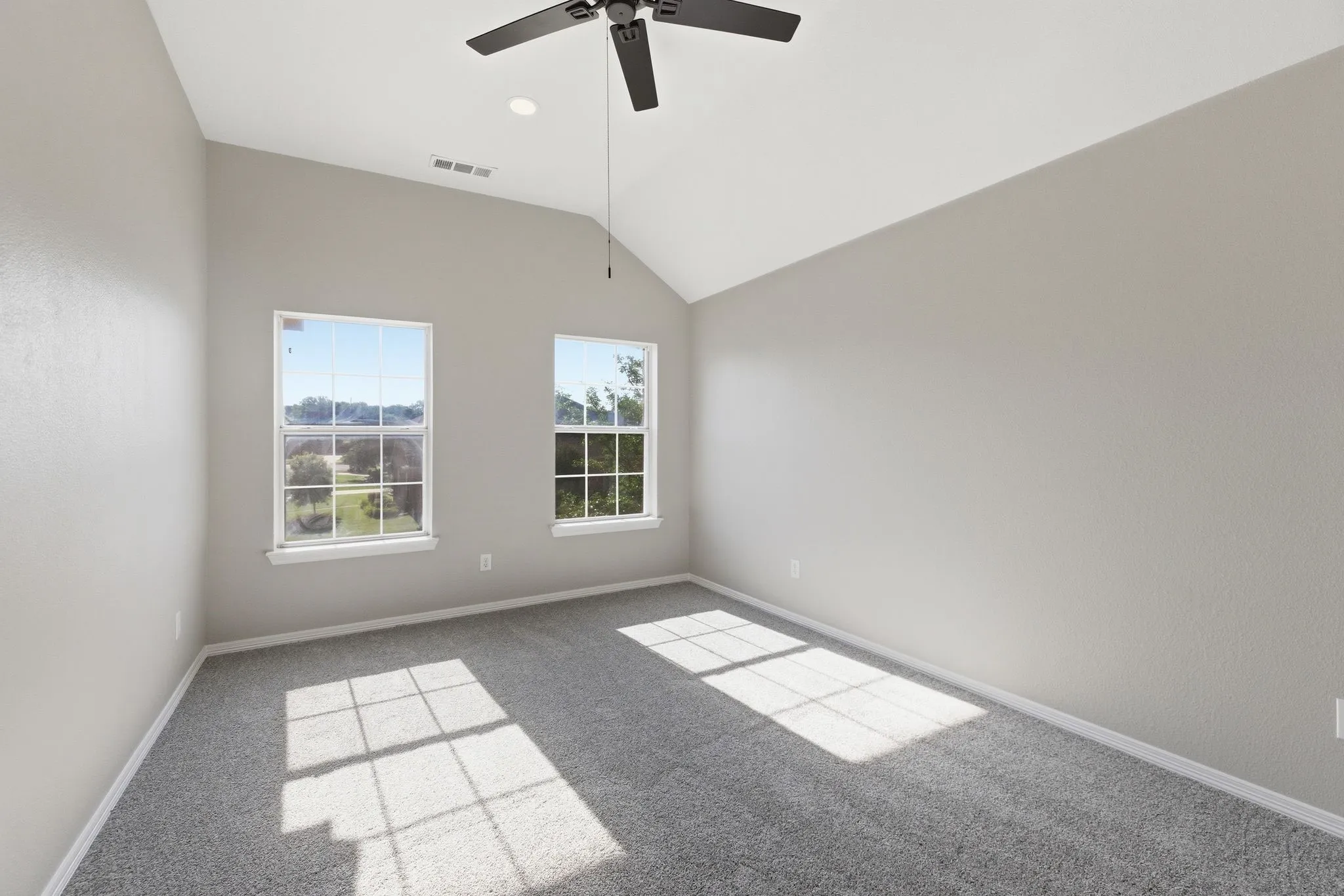 Spacious room with vaulted ceilings, two double-hung windows, light gray textured walls, and gray carpeting