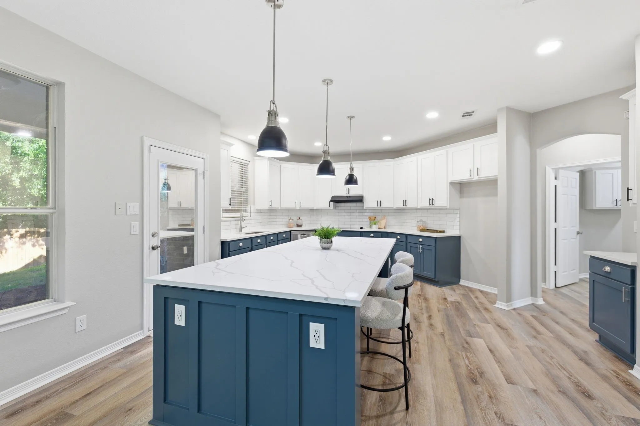 Spacious kitchen featuring a large island with a patterned countertop, two-tone cabinetry, wood-finish flooring, recessed lighting, and pendant fixtures