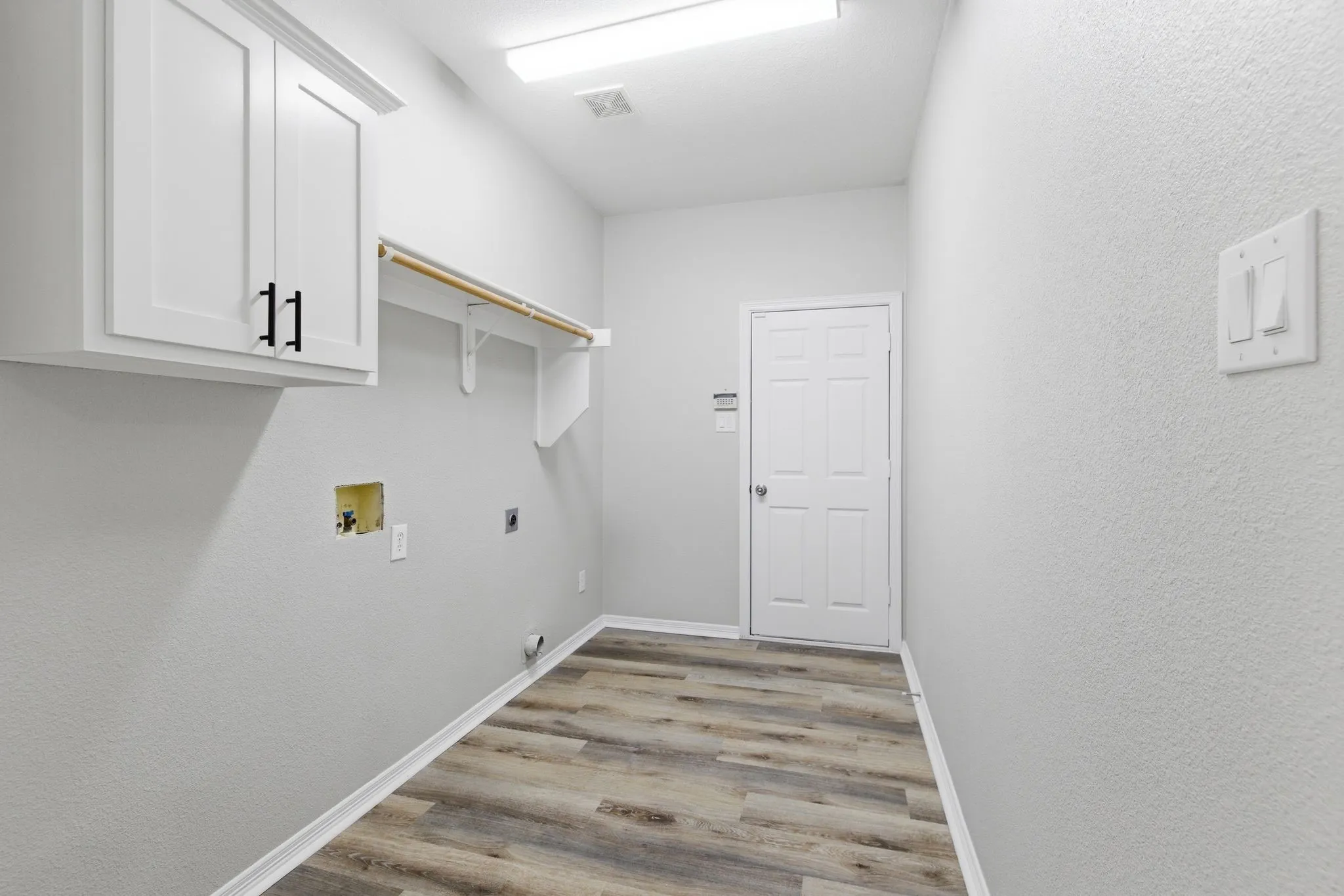 Laundry area featuring wood-finish flooring, white cabinetry with black hardware, a built-in hanging rod, and light-colored walls