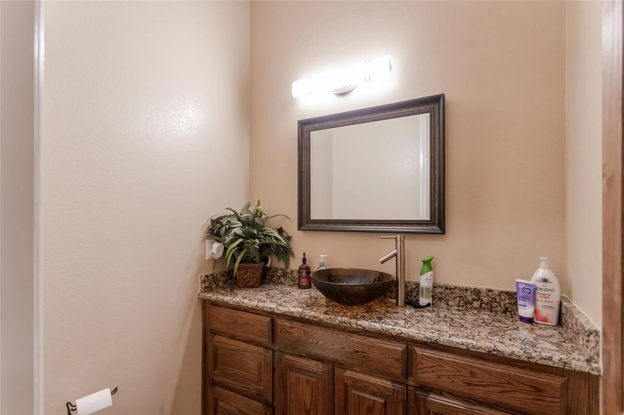 Wood-finish vanity with panel-front cabinetry, granite-style countertop, and vessel sink with a brushed nickel faucet