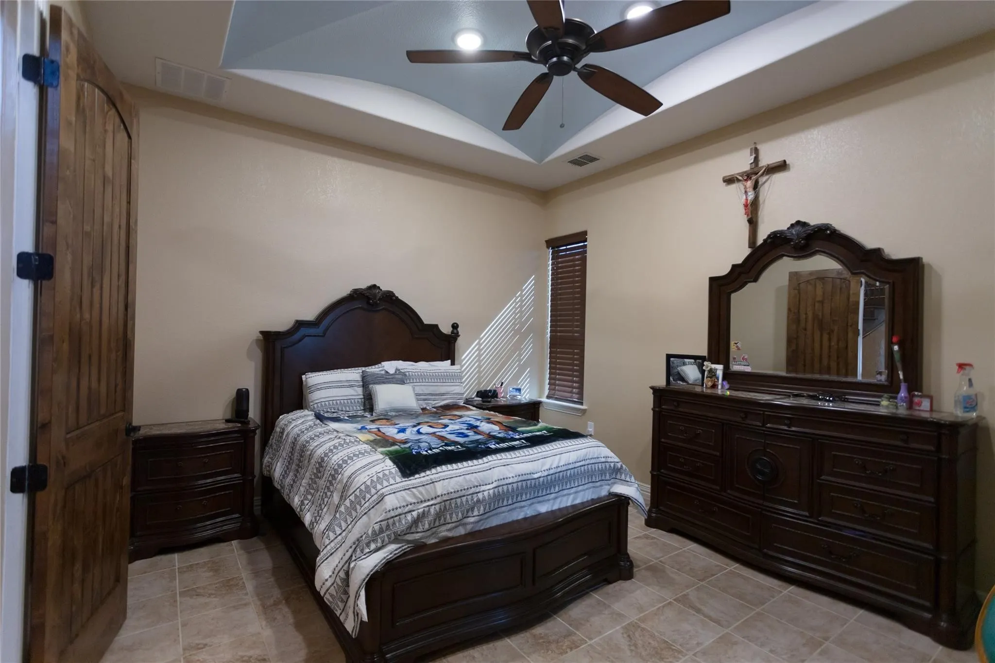 Tray ceiling with recessed lighting and a ceiling fan, wood-finish paneled door with dark hardware, tiled flooring, and a window with blinds