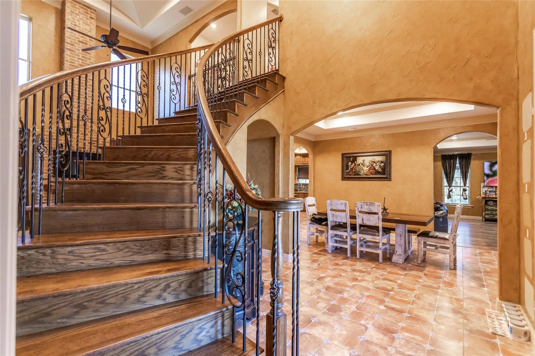 Curved staircase with wood treads and wrought iron balusters, arched doorways, and tile flooring