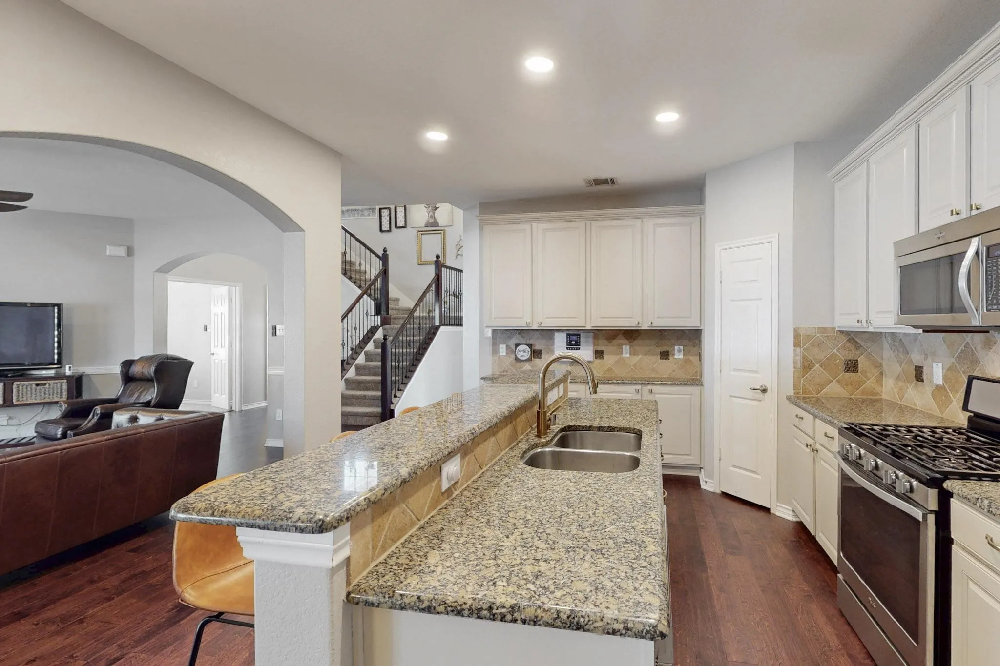 Spacious kitchen featuring an expansive granite island with a double basin sink, stainless steel appliances, and white cabinetry
