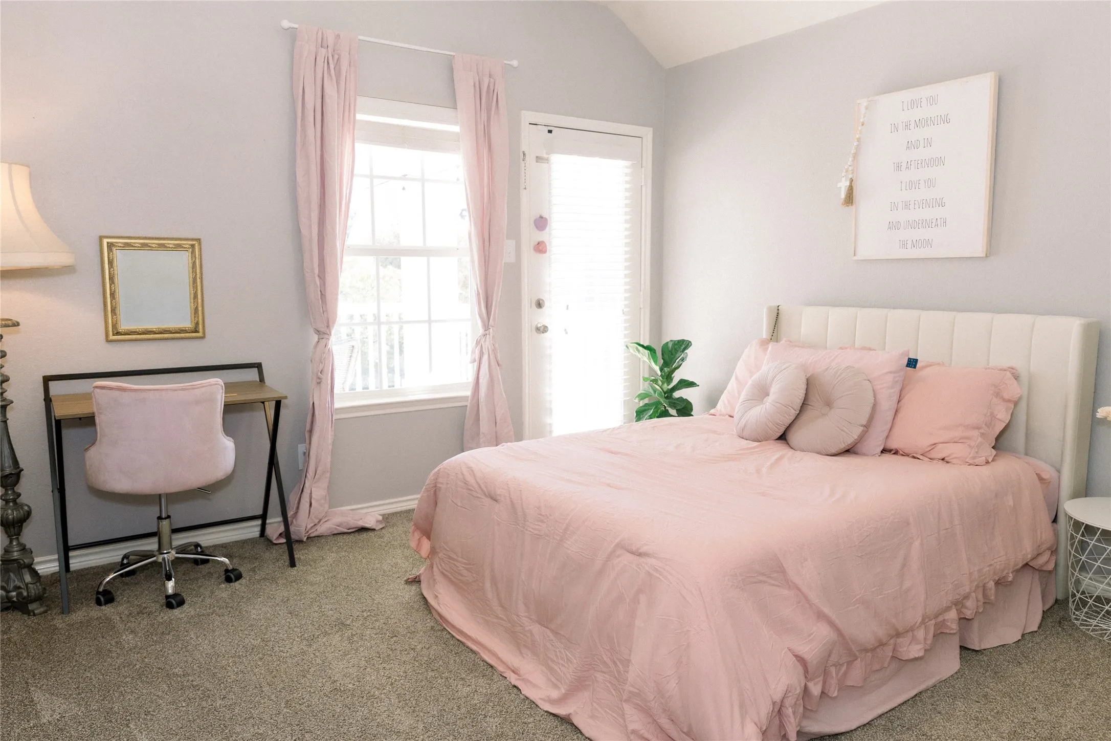 Vaulted ceiling, carpet flooring, window with white trim, and a door with louvered blinds