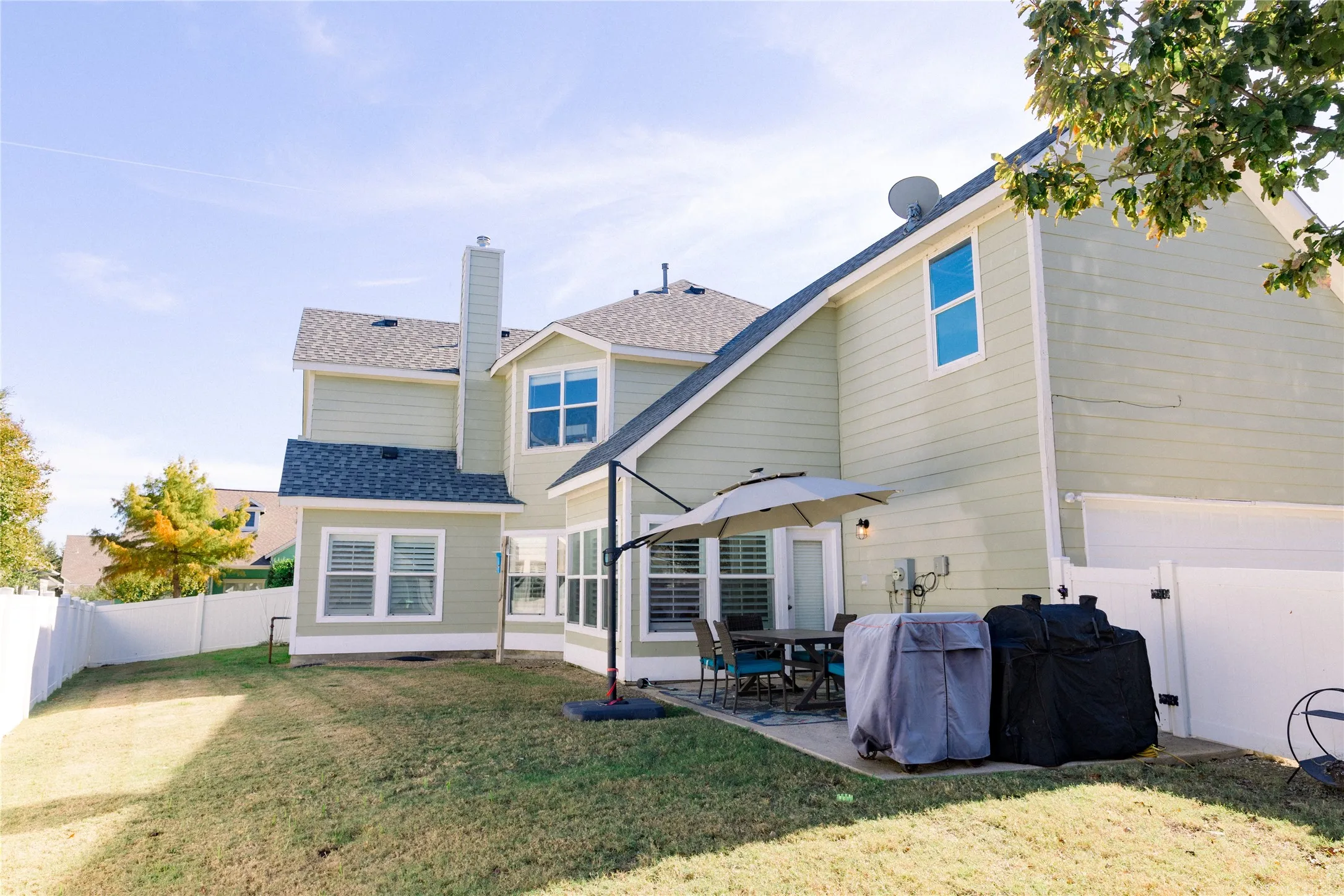 Expansive backyard featuring a manicured lawn, a concrete patio, and a white privacy fence