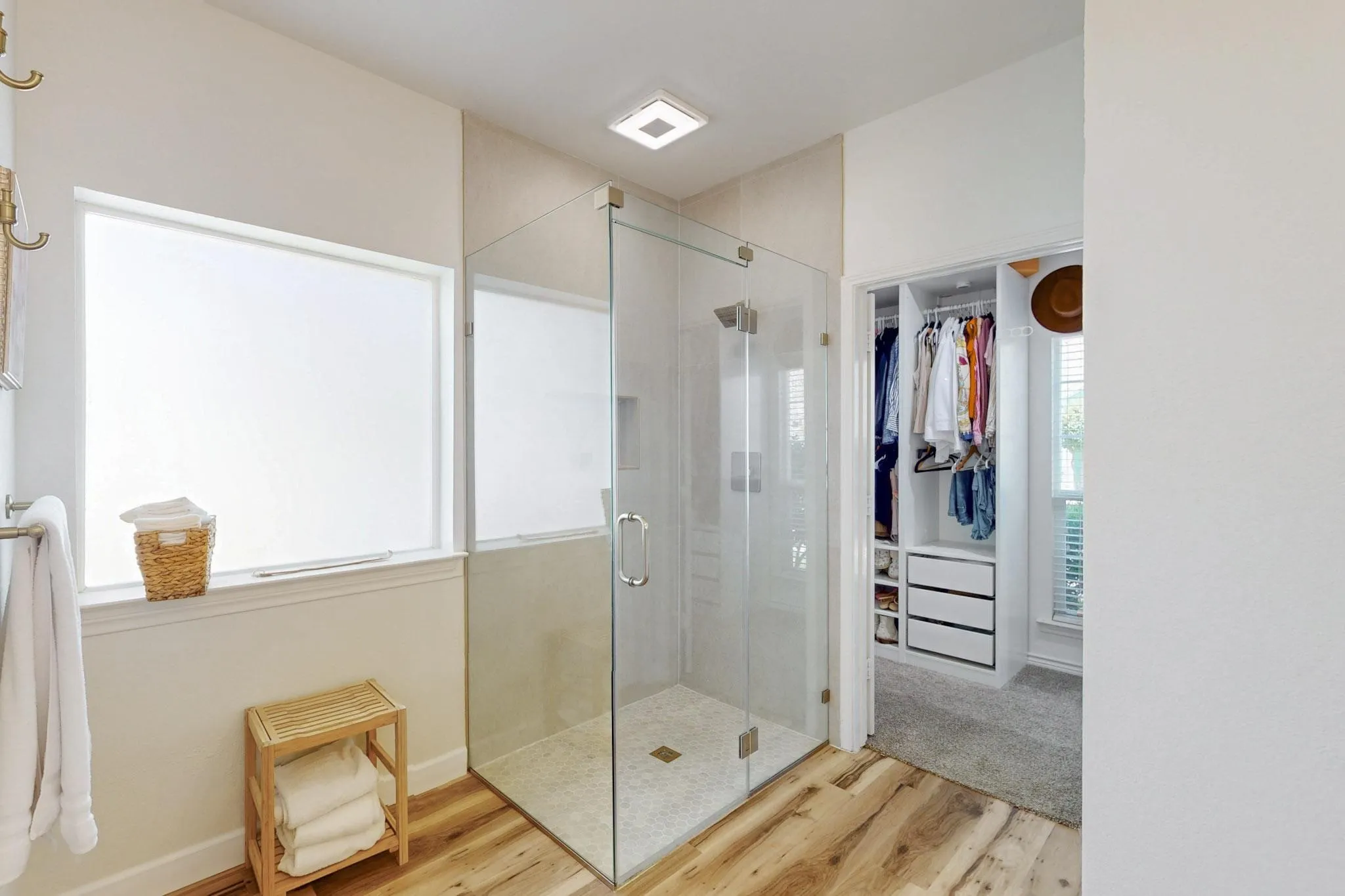 Glass-enclosed shower with stone tile, wood-finish flooring, and a custom closet system