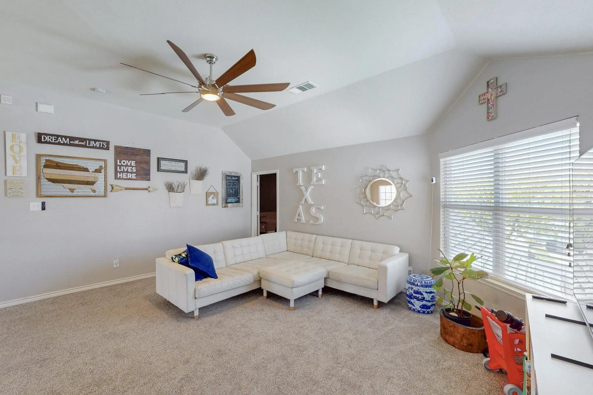 Vaulted ceiling with an installed ceiling fan, carpeted flooring, and a large window with horizontal blinds
