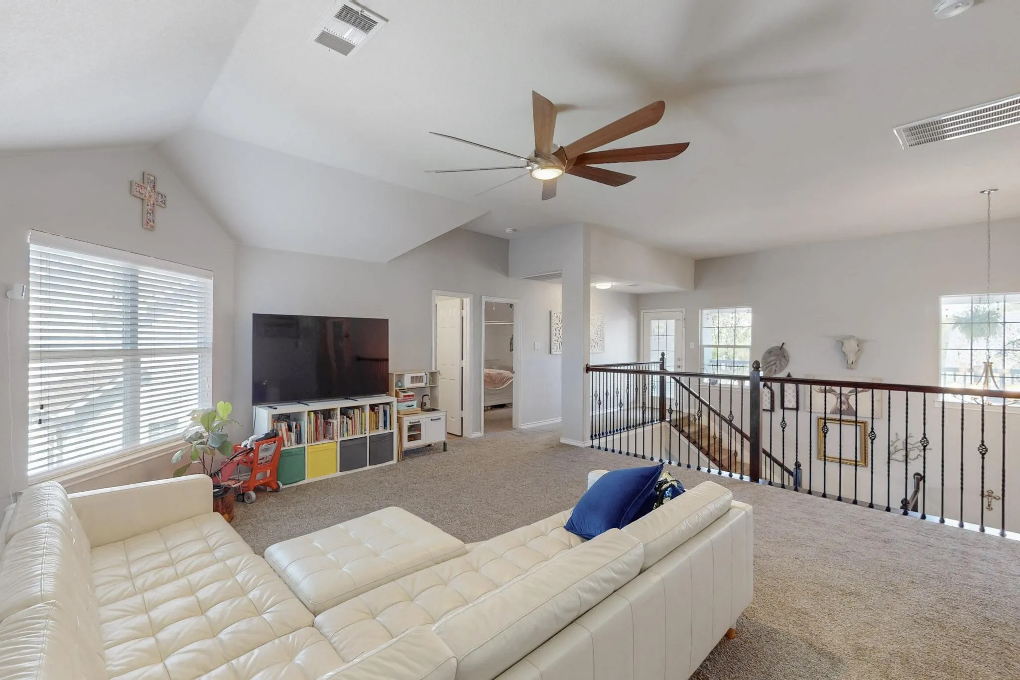 Carpeted loft area featuring a vaulted ceiling with a ceiling fan, multiple windows with blinds, and a built-in railing overlooking the lower level
