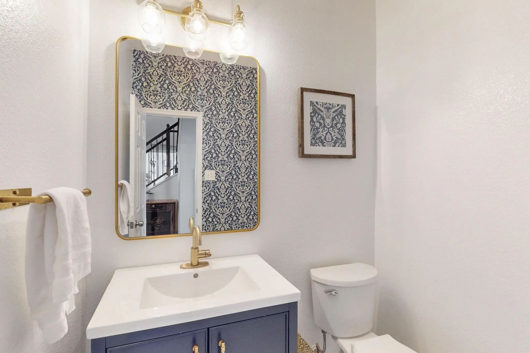 Downstairs half bathroom Vanity with a white countertop and blue cabinetry, brass-finish faucet, and coordinating brass-finish mirror
