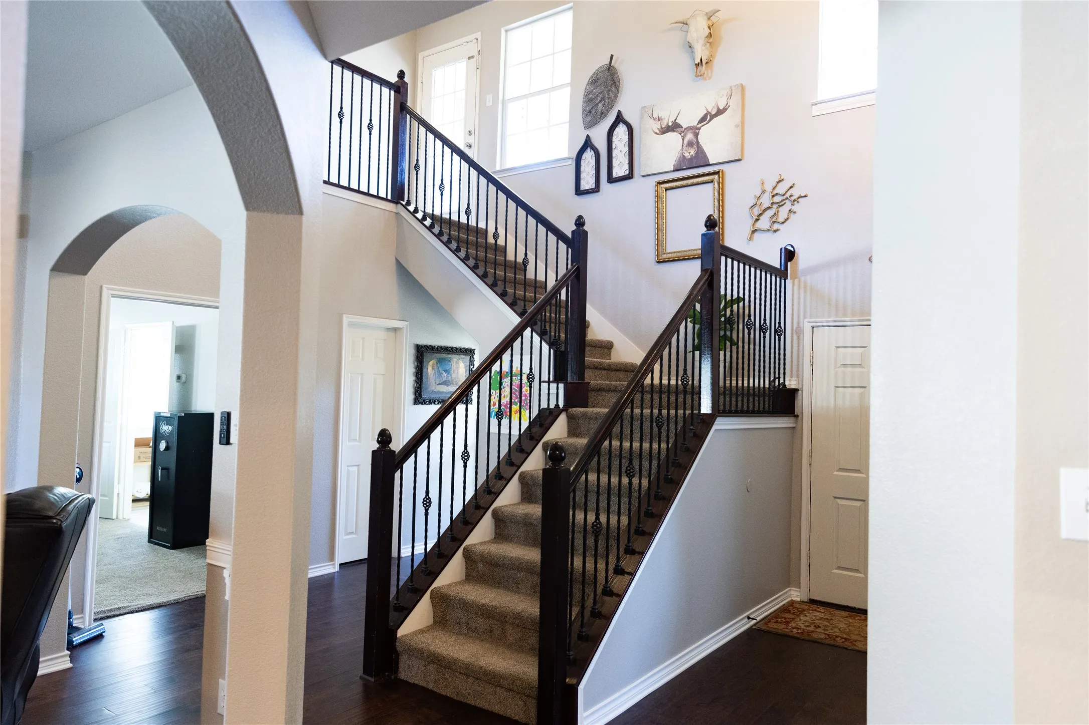 Grand foyer with wood-finish flooring, a two-story staircase featuring dark wood newel posts and wrought iron balusters, and arched doorways