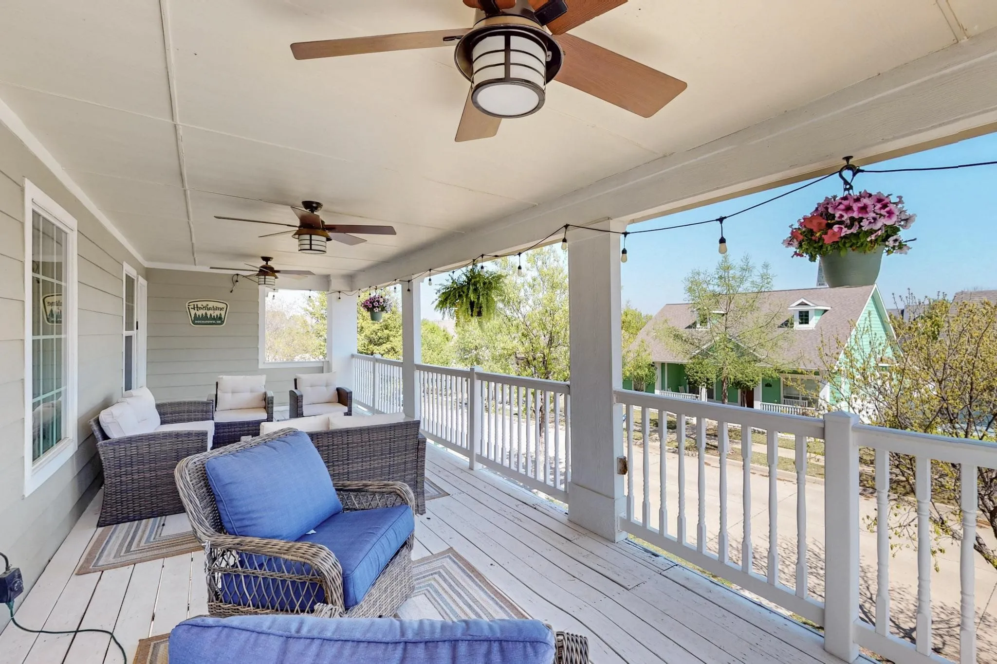 Expansive covered porch featuring a painted wood-finish deck, multiple ceiling fans, and string lighting