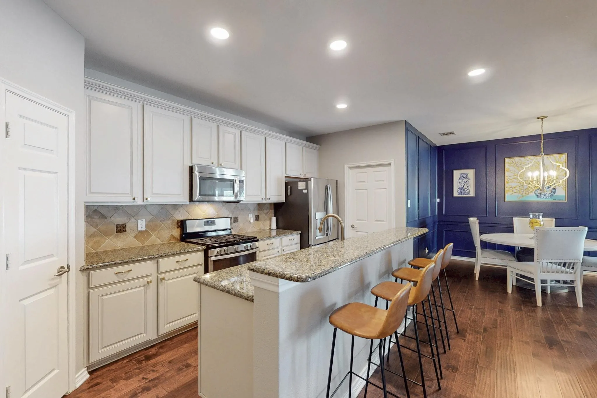 Kitchen featuring white cabinetry, granite countertops, tile backsplash, stainless steel appliances, and wood-finish flooring