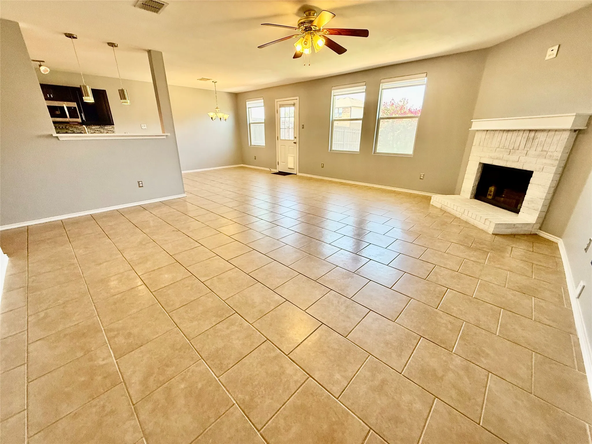 Expansive tile flooring, white brick fireplace, ceiling fan, and multiple windows
