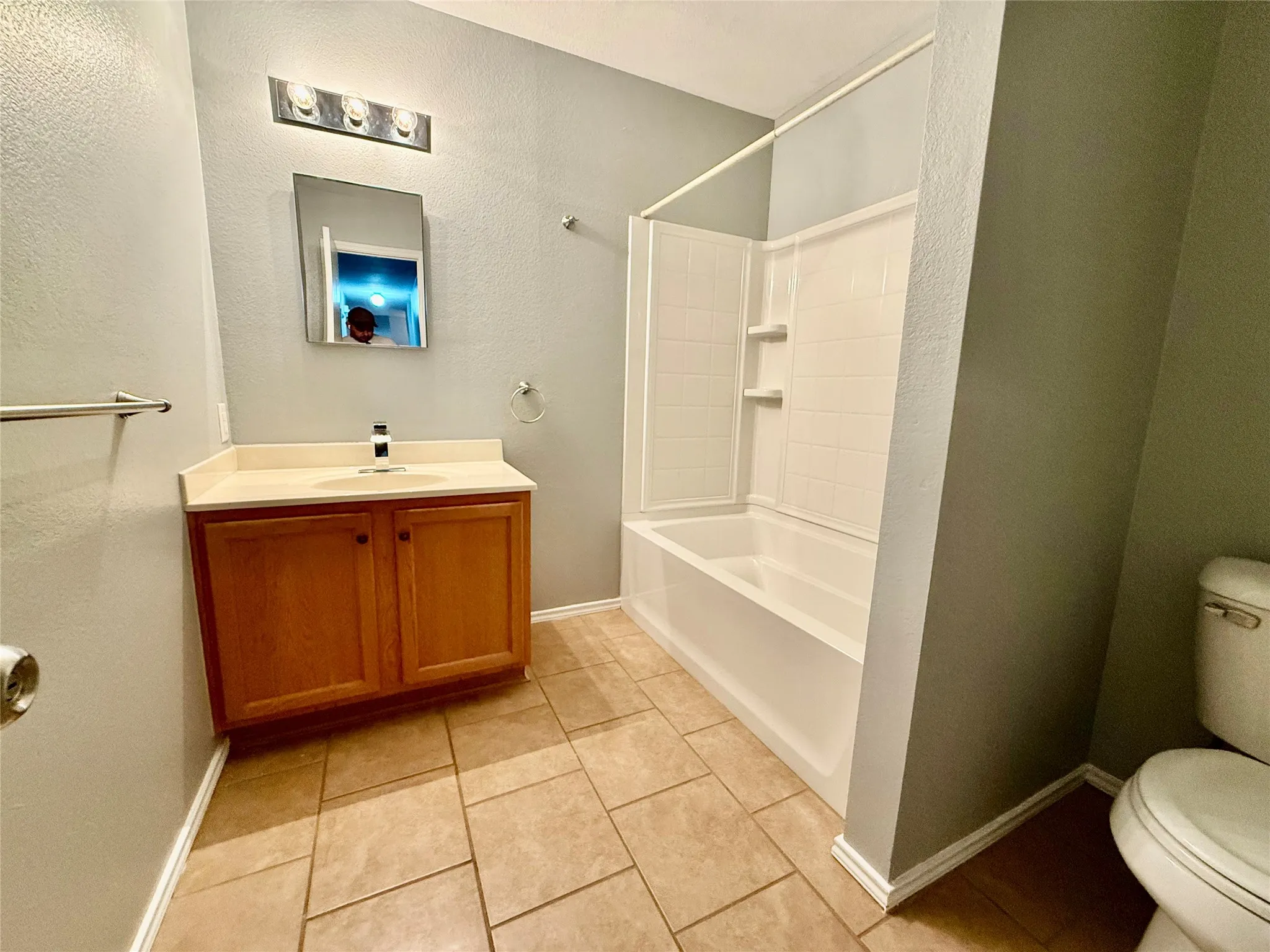 Bathroom featuring a wood-finish vanity with an integrated sink, a built-in tub with shower, tiled flooring, and a mirrored medicine cabinet