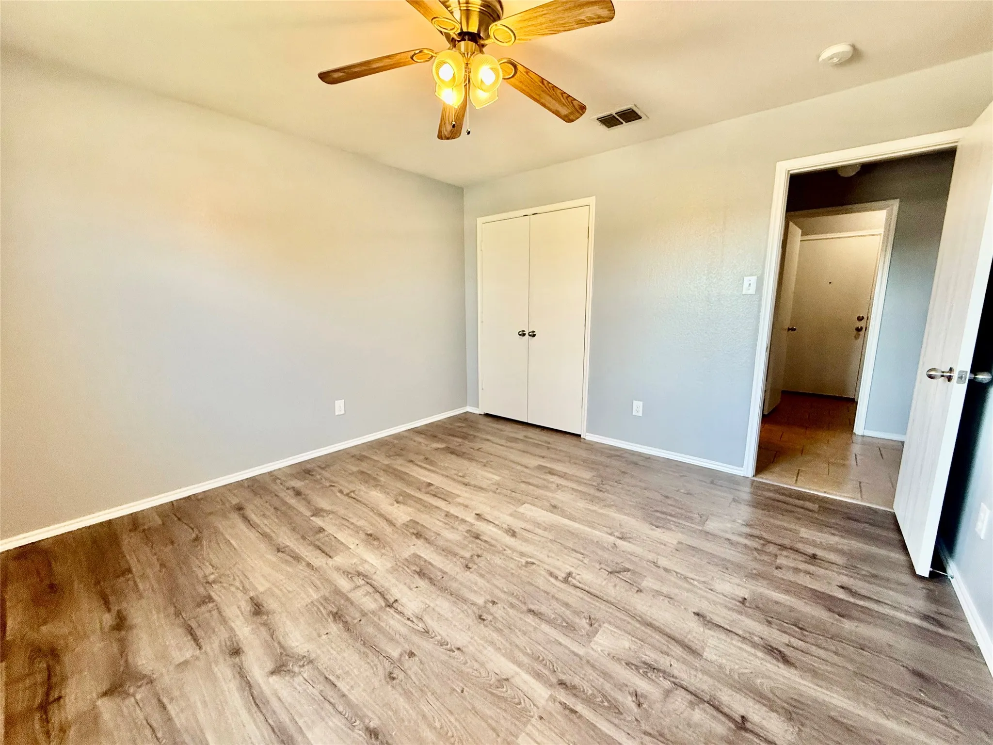Wood-finish flooring, ceiling fan with integrated lighting, and a double-door closet