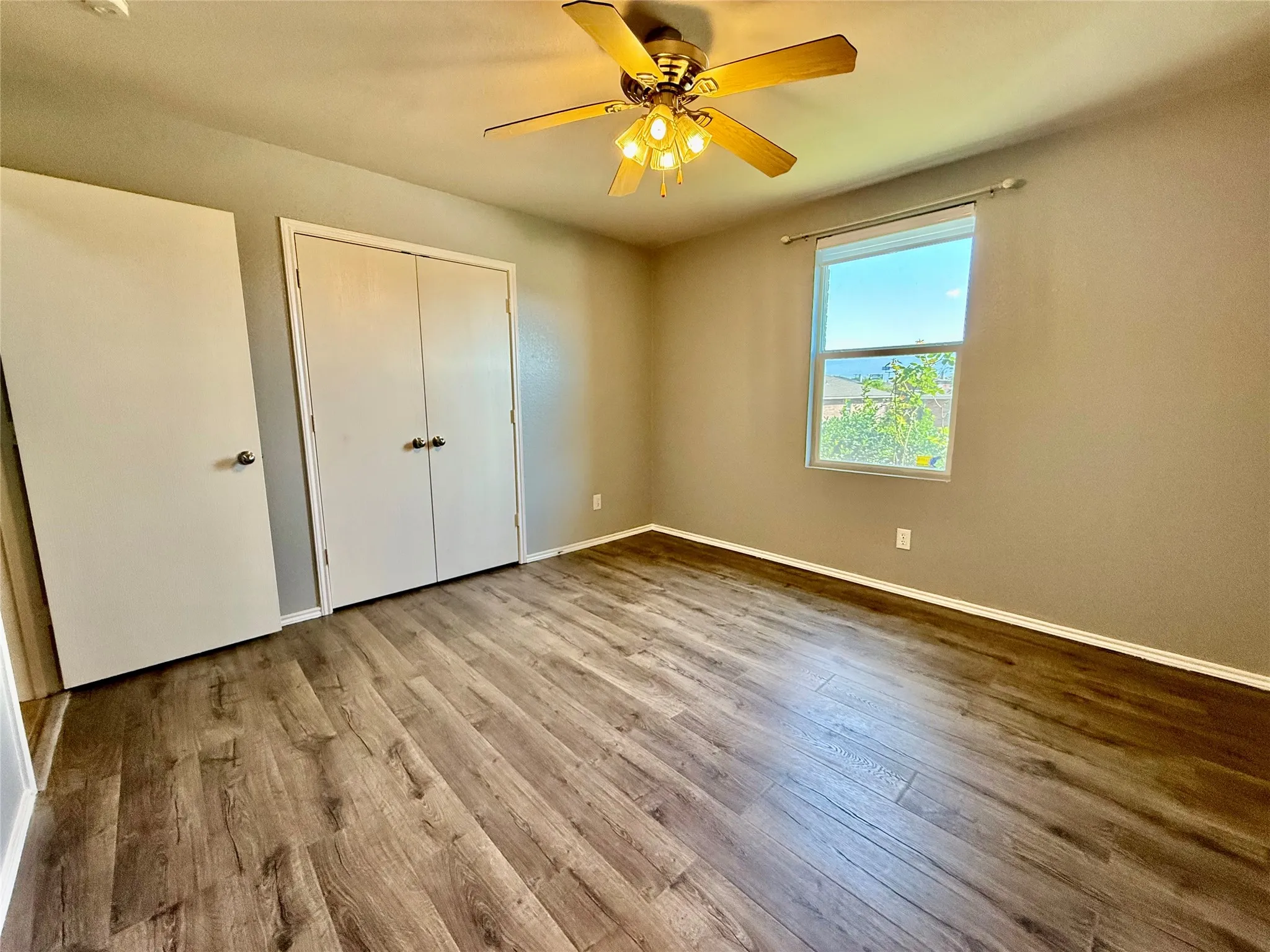 Wood-finish flooring, ceiling fan with integrated lighting, window with a white frame, and a double-door closet