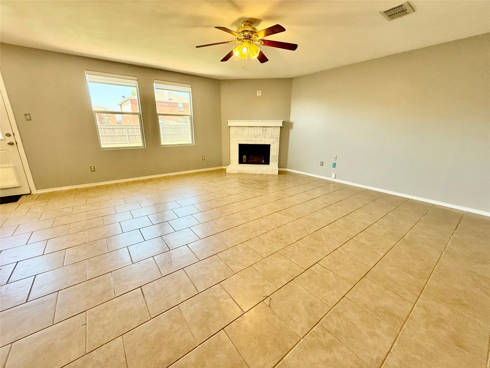 Ceramic tile flooring, white-painted fireplace with mantel, two windows, and a ceiling fan with integrated lighting