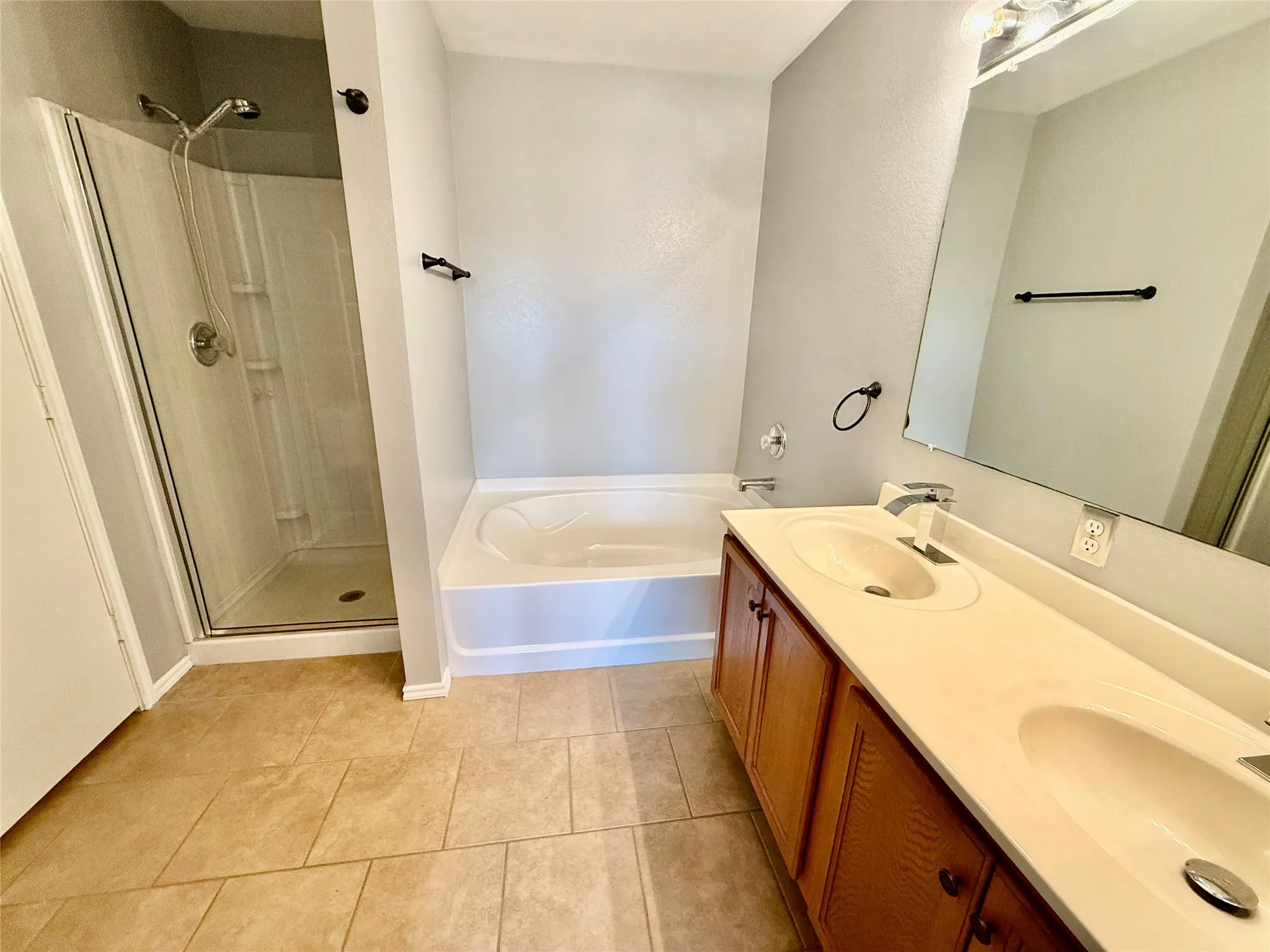 Dual vanity with integrated sinks, a built-in bathtub, a separate walk-in shower with a glass enclosure, and large format tile flooring