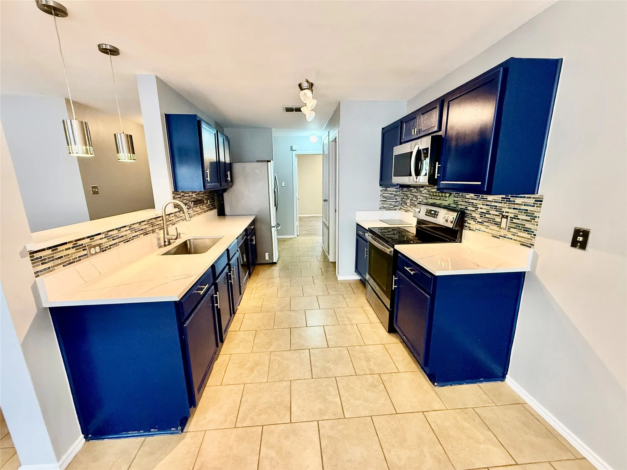 Kitchen featuring sleek blue cabinetry, light-toned countertops, a mosaic tile backsplash, stainless steel appliances, and tiled flooring