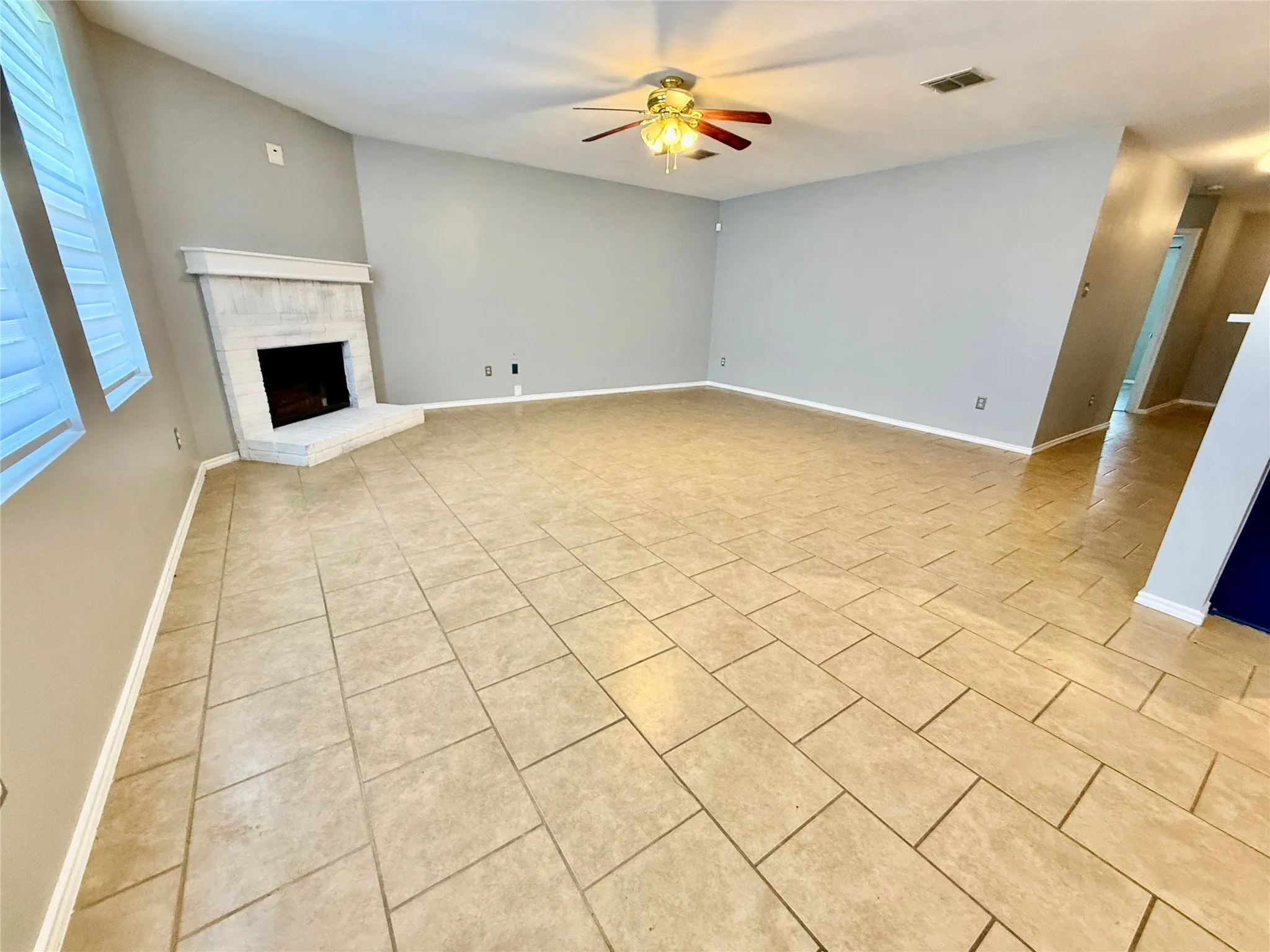 Expansive living area featuring tile flooring, a corner fireplace with a white mantel, light gray wall paint, and a ceiling fan with integrated lighting