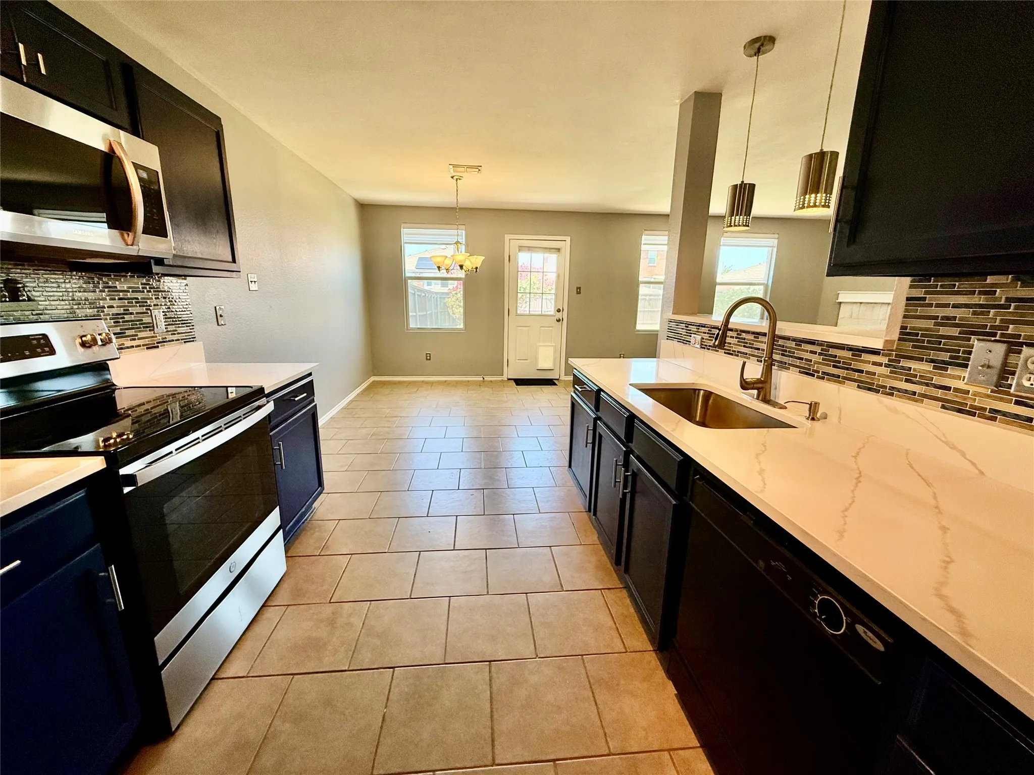 Kitchen featuring dark cabinetry, light countertops, a stainless steel sink, a tile backsplash, and tile flooring