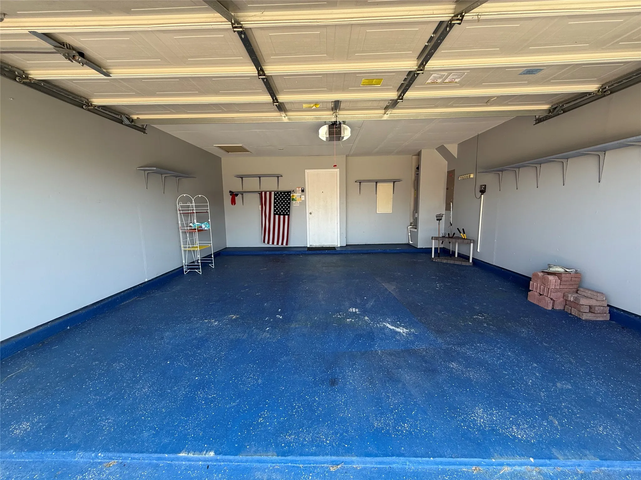 Garage featuring a blue-finished floor, white paneled garage door, and built-in wall shelving