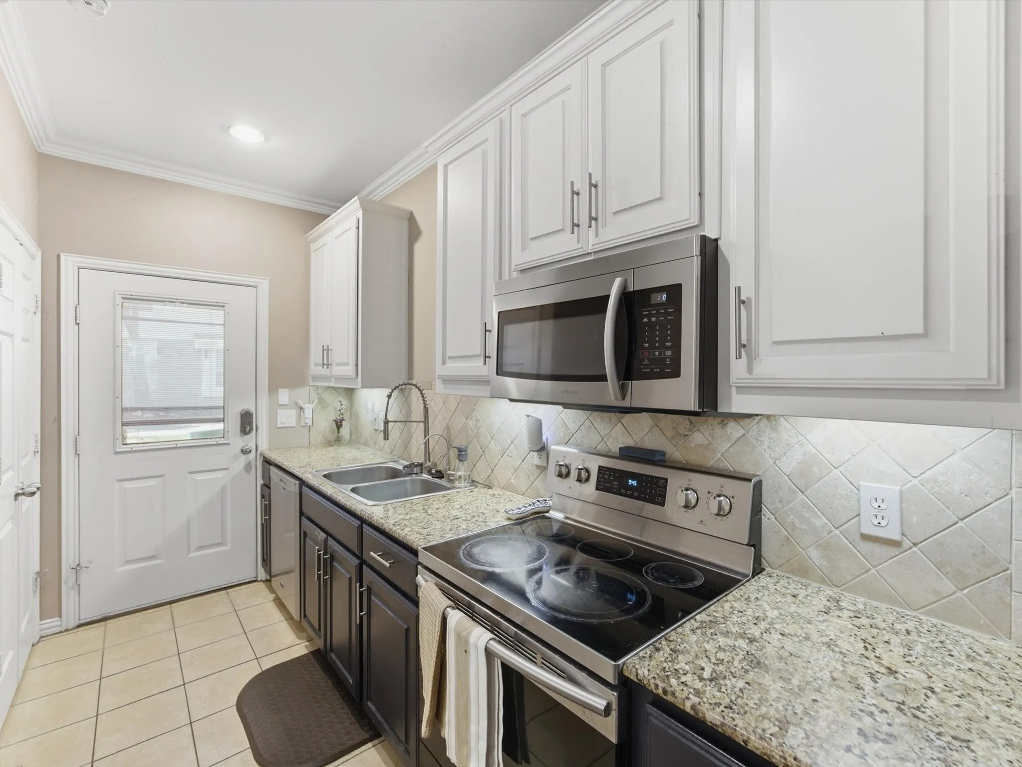Kitchen featuring stainless steel appliances, dual-tone cabinetry, tiled flooring, speckled countertops, and a tiled backsplash