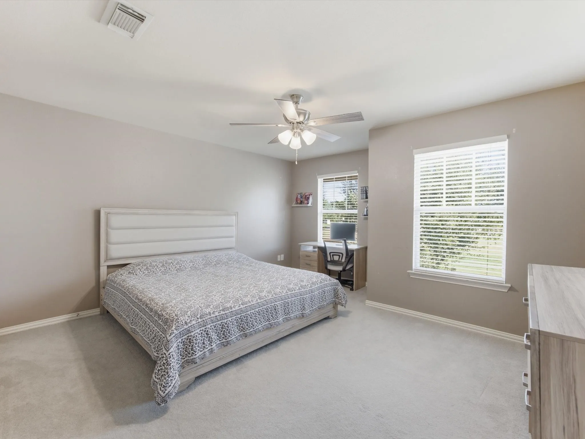 Carpeted flooring, neutral wall tones, window with white blinds, ceiling fan with integrated lighting, and a built-in desk area