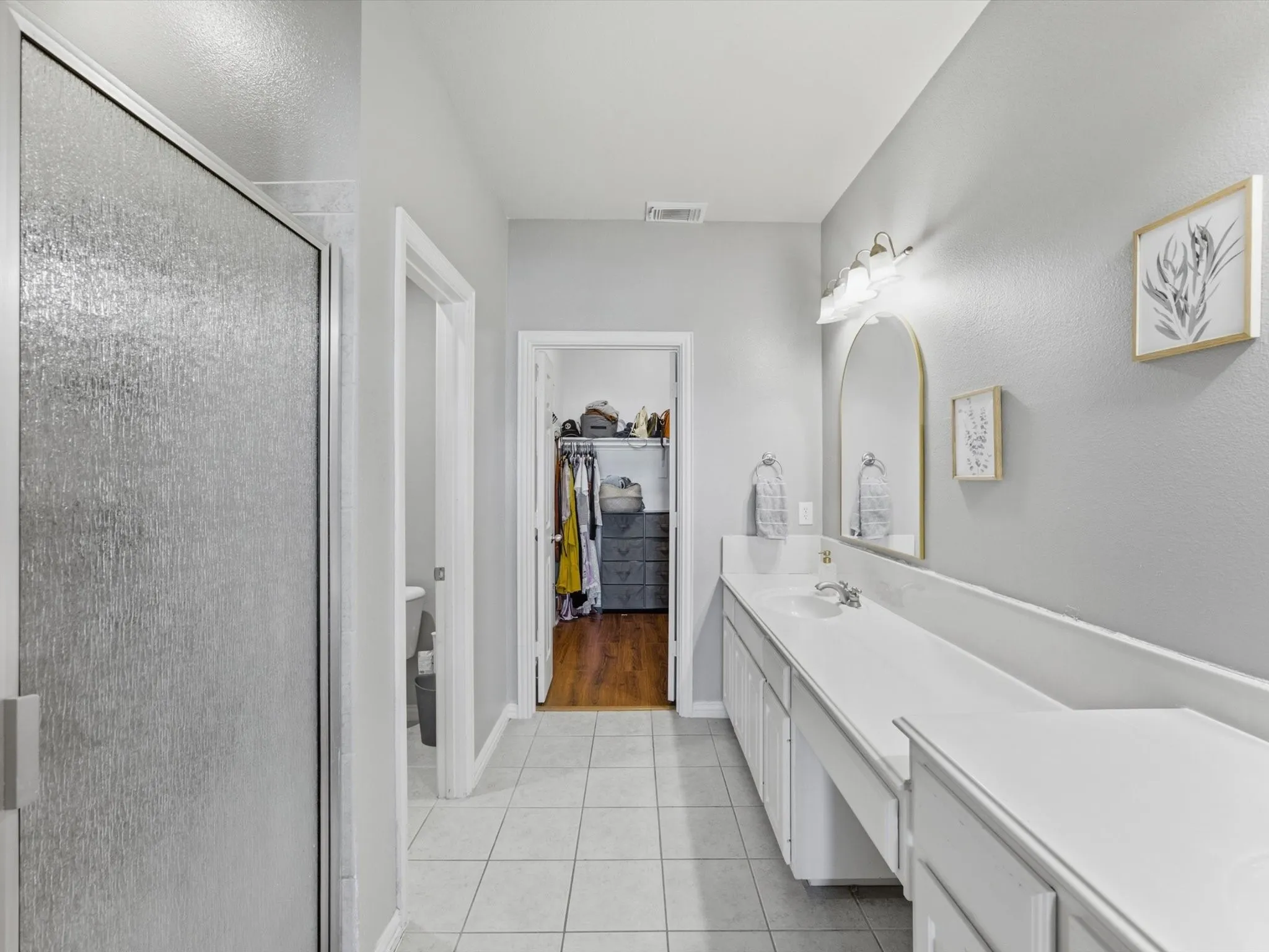 Frosted glass shower enclosure, vanity with dual sinks, white cabinetry, tile flooring, and wall-mounted lighting