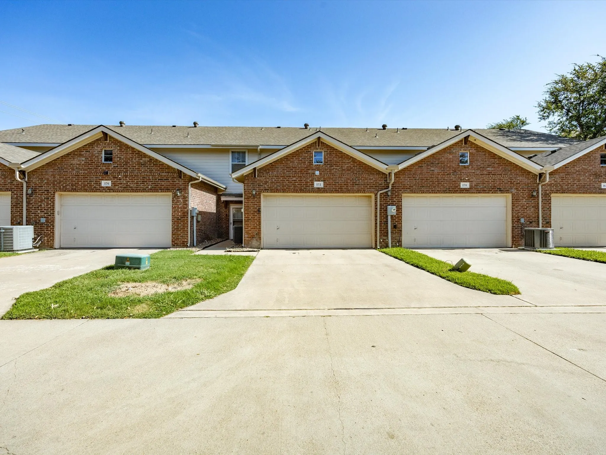 Brick facade, individual garage doors, dedicated driveways, pitched roofing, visible HVAC units