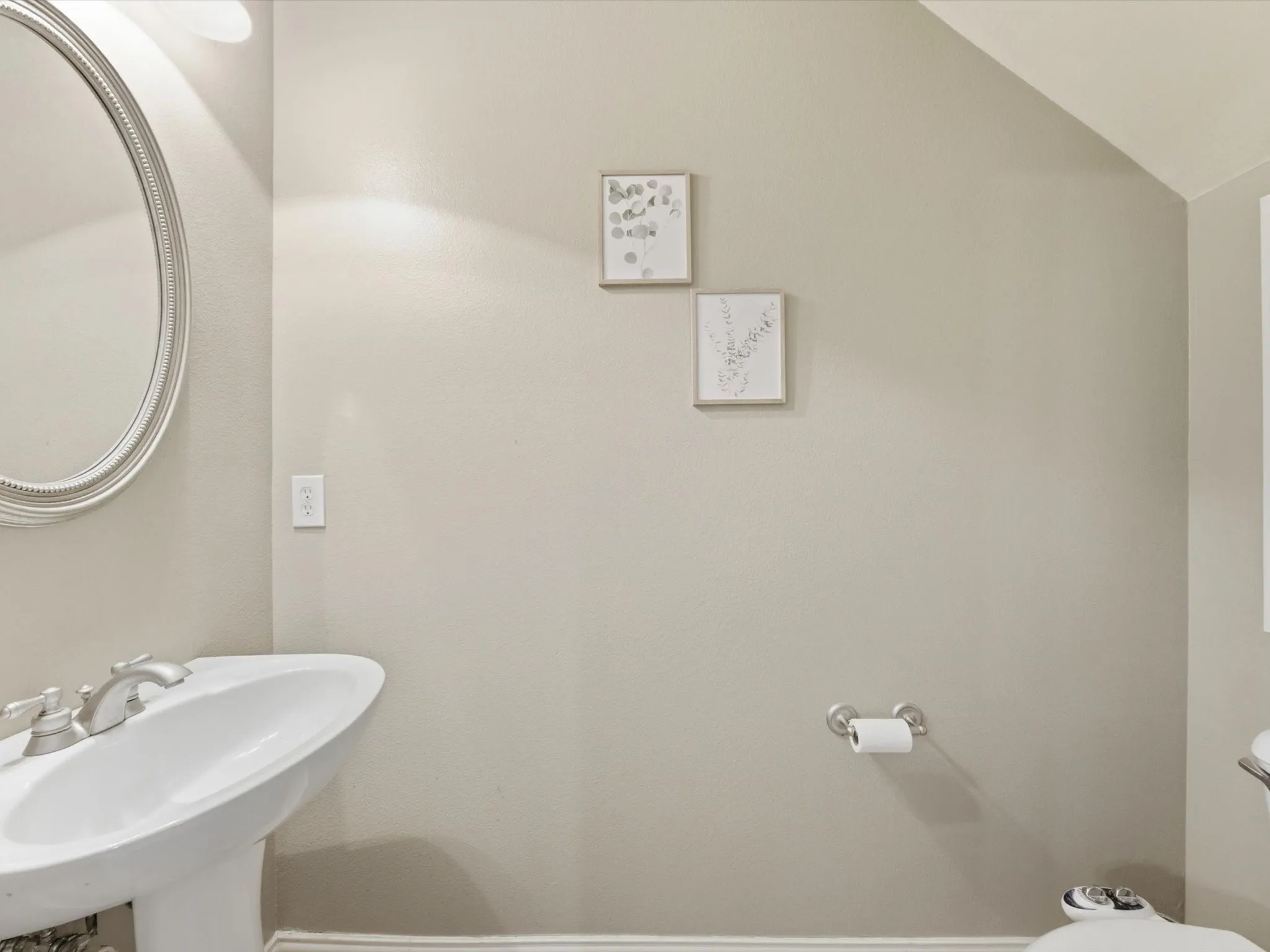 Pedestal sink with a polished chrome faucet, an oval mirror with a decorative frame, and a wall-mounted light fixture