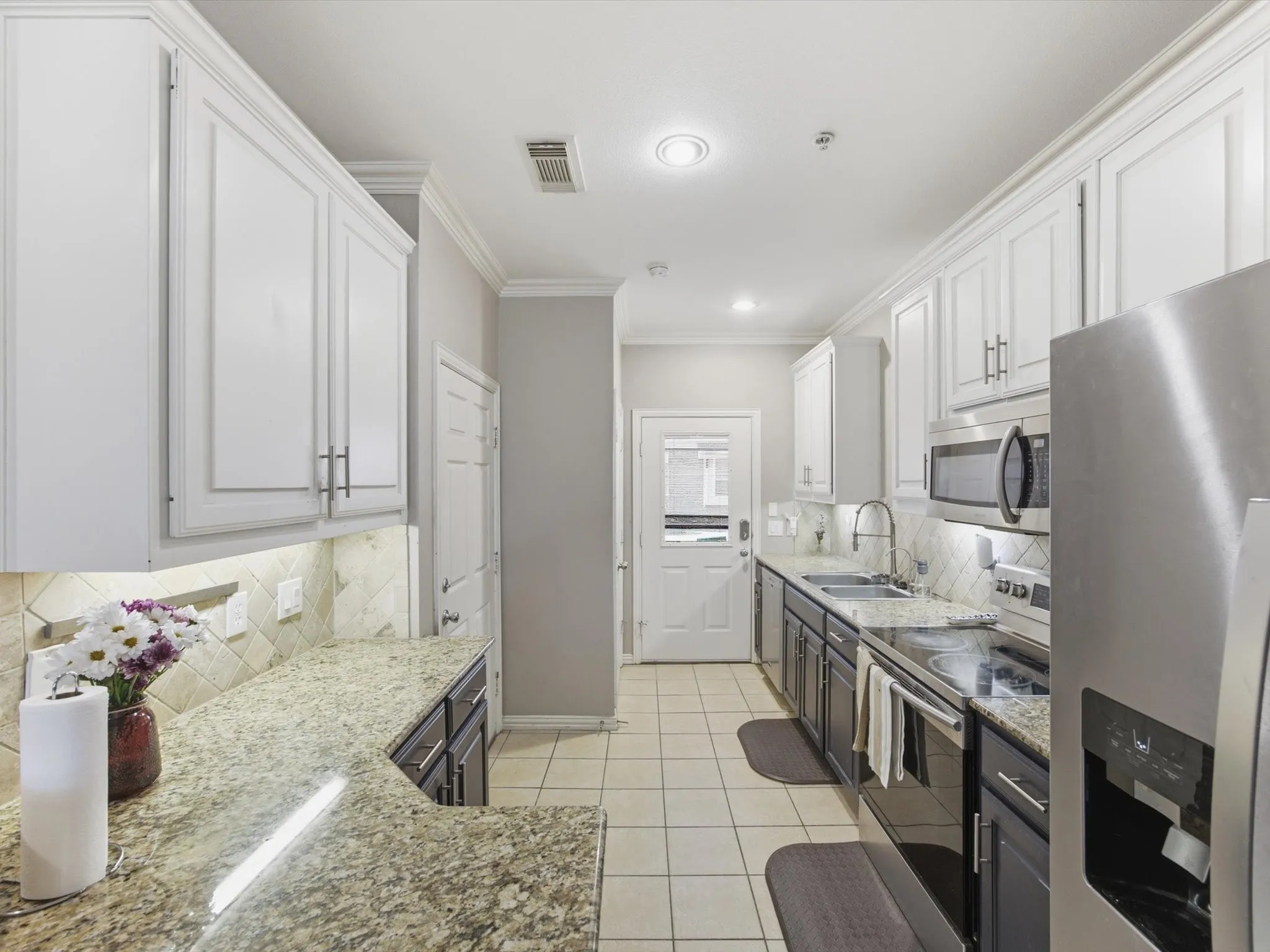 Galley kitchen featuring dual-toned cabinetry, stainless steel appliances, granite countertops, and tile flooring
