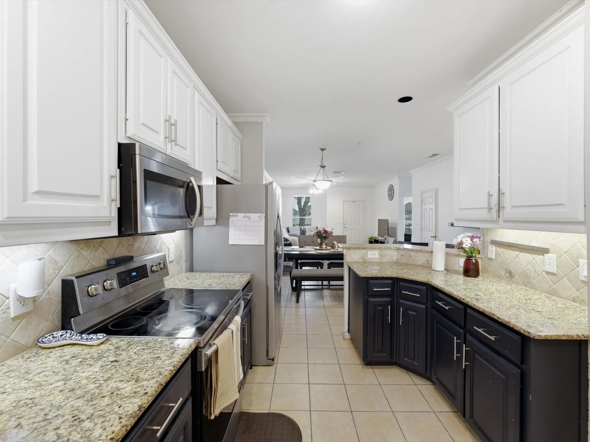 Kitchen featuring white upper cabinetry, dark lower cabinetry, light-toned countertops, stainless steel appliances, and a tiled backsplash