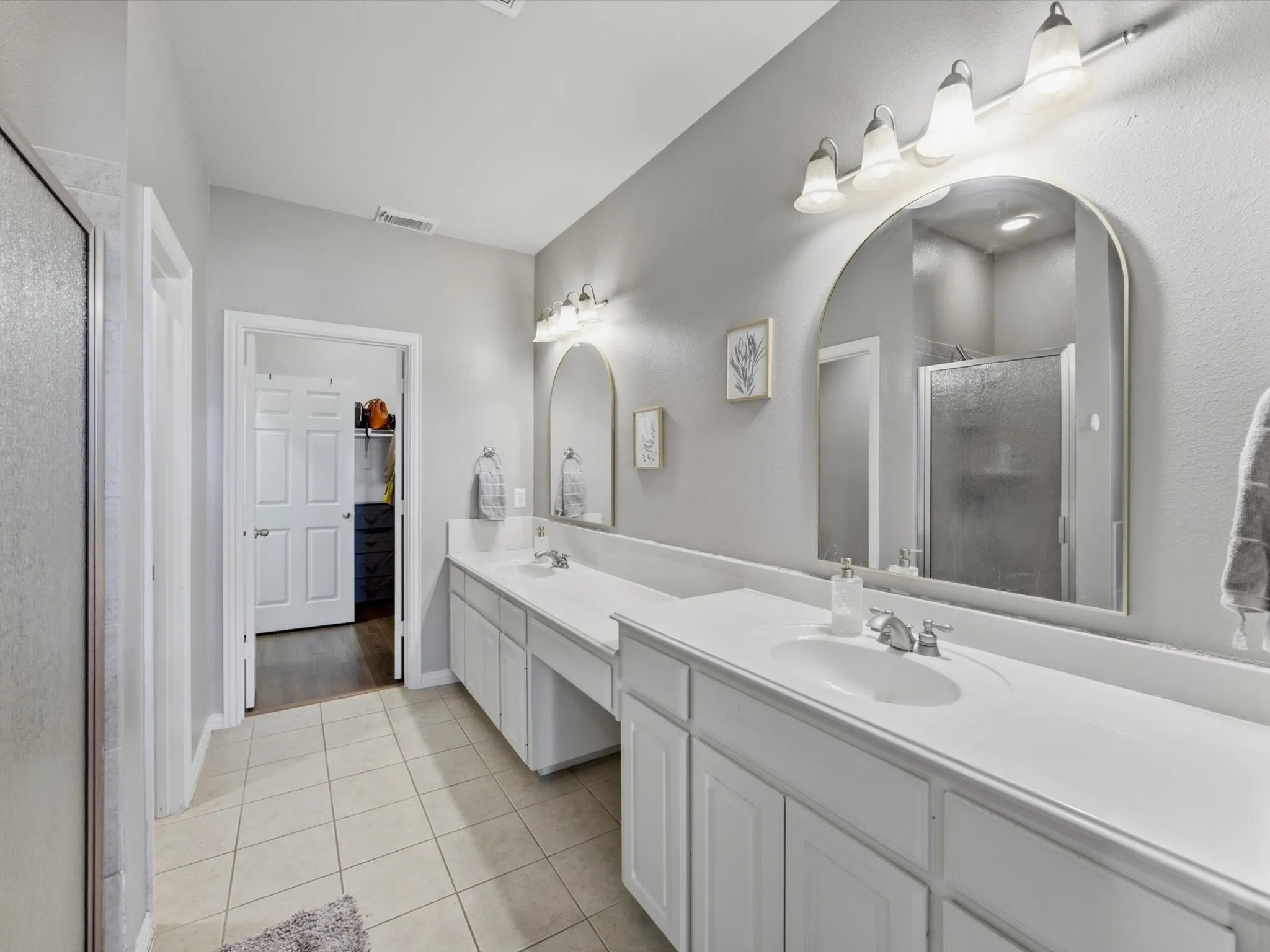 Dual vanity with white cabinetry, integrated sinks, chrome fixtures, and arched mirrors