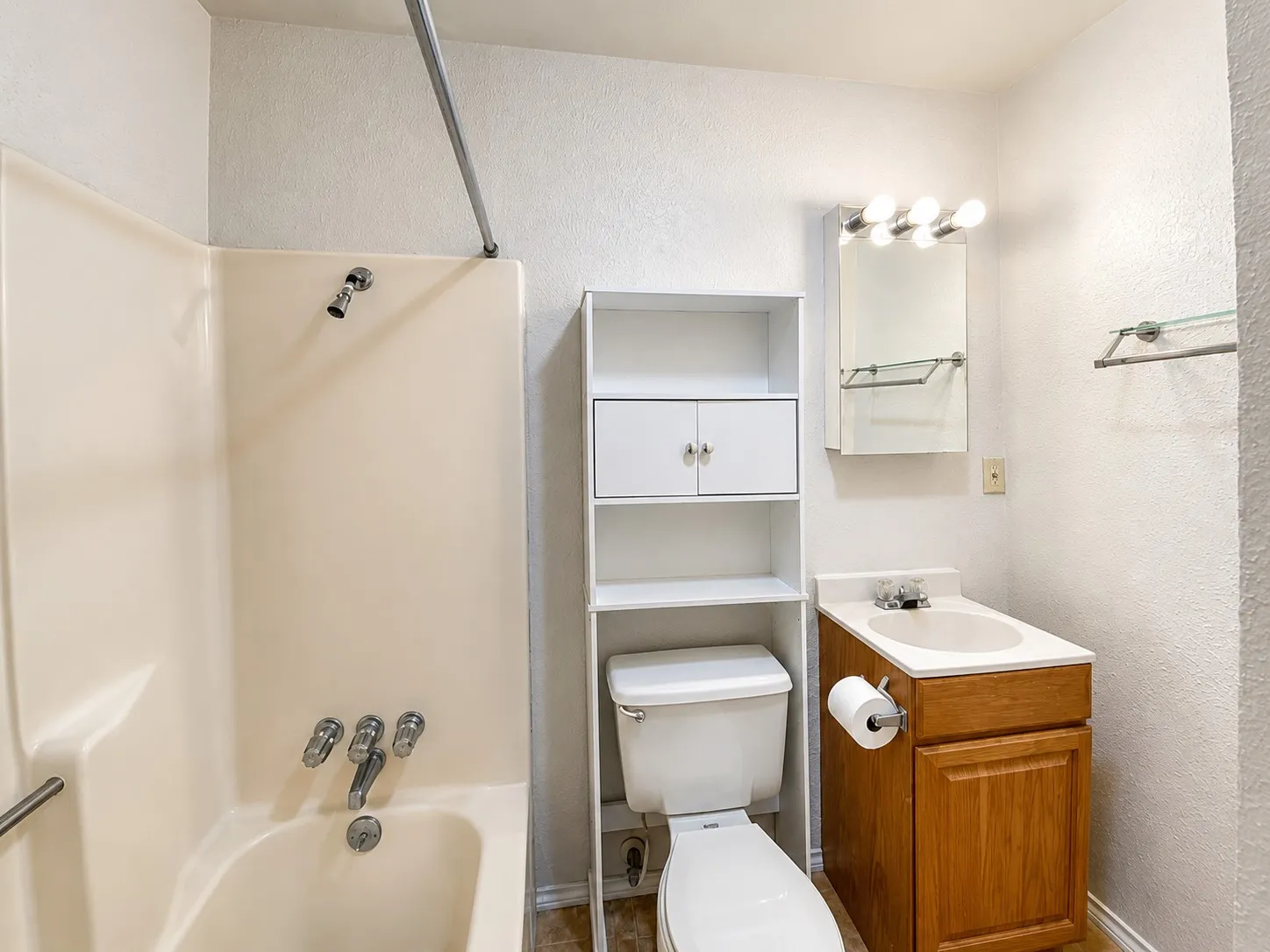 Functional bathroom featuring a wood-finish vanity with integrated sink, ceramic tile walls, recessed medicine cabinet with mirror, toilet, and overhead lighting