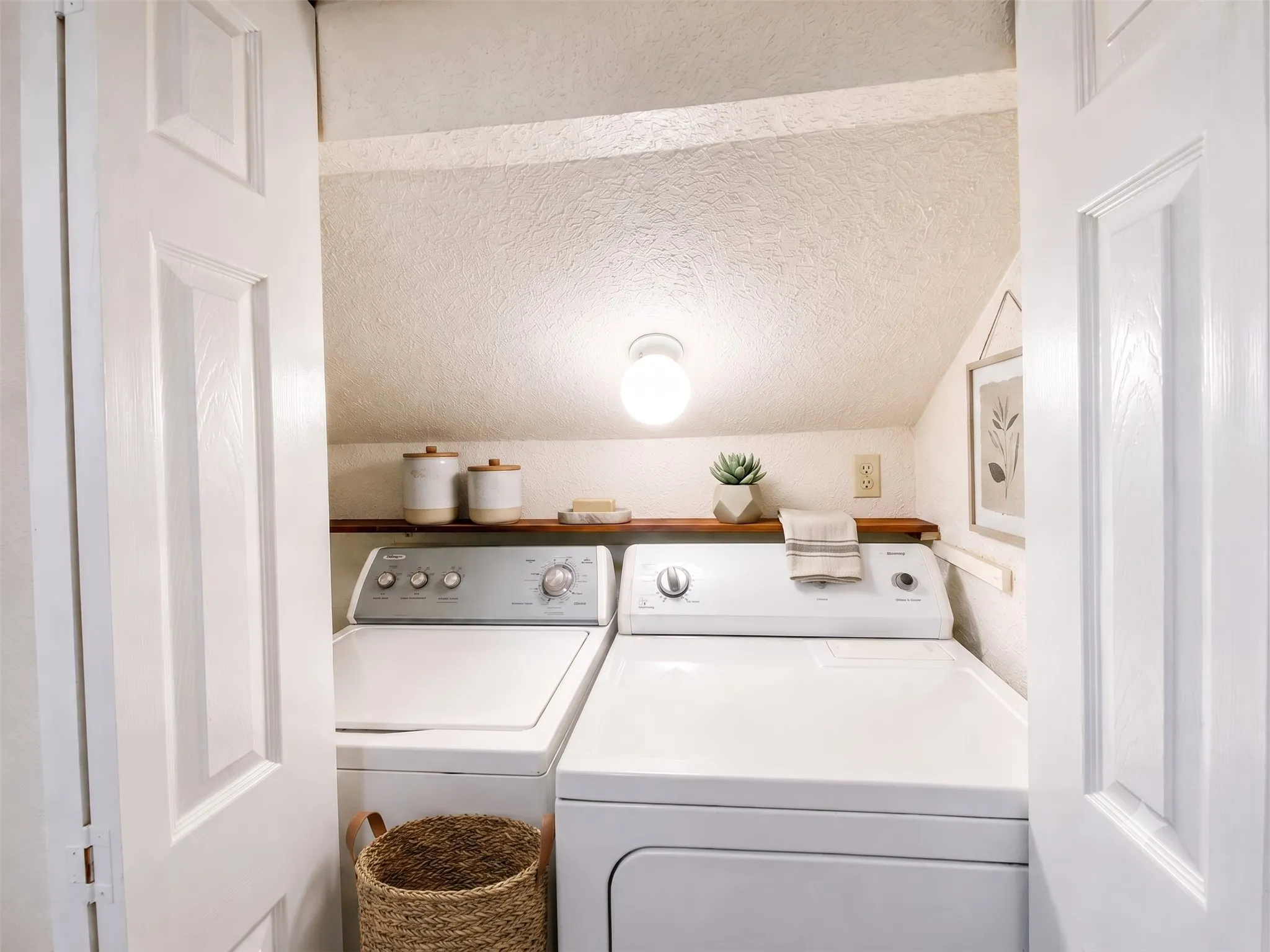 Dedicated laundry area featuring a shelf, overhead lighting, and white paneled doors-Virtually Staged