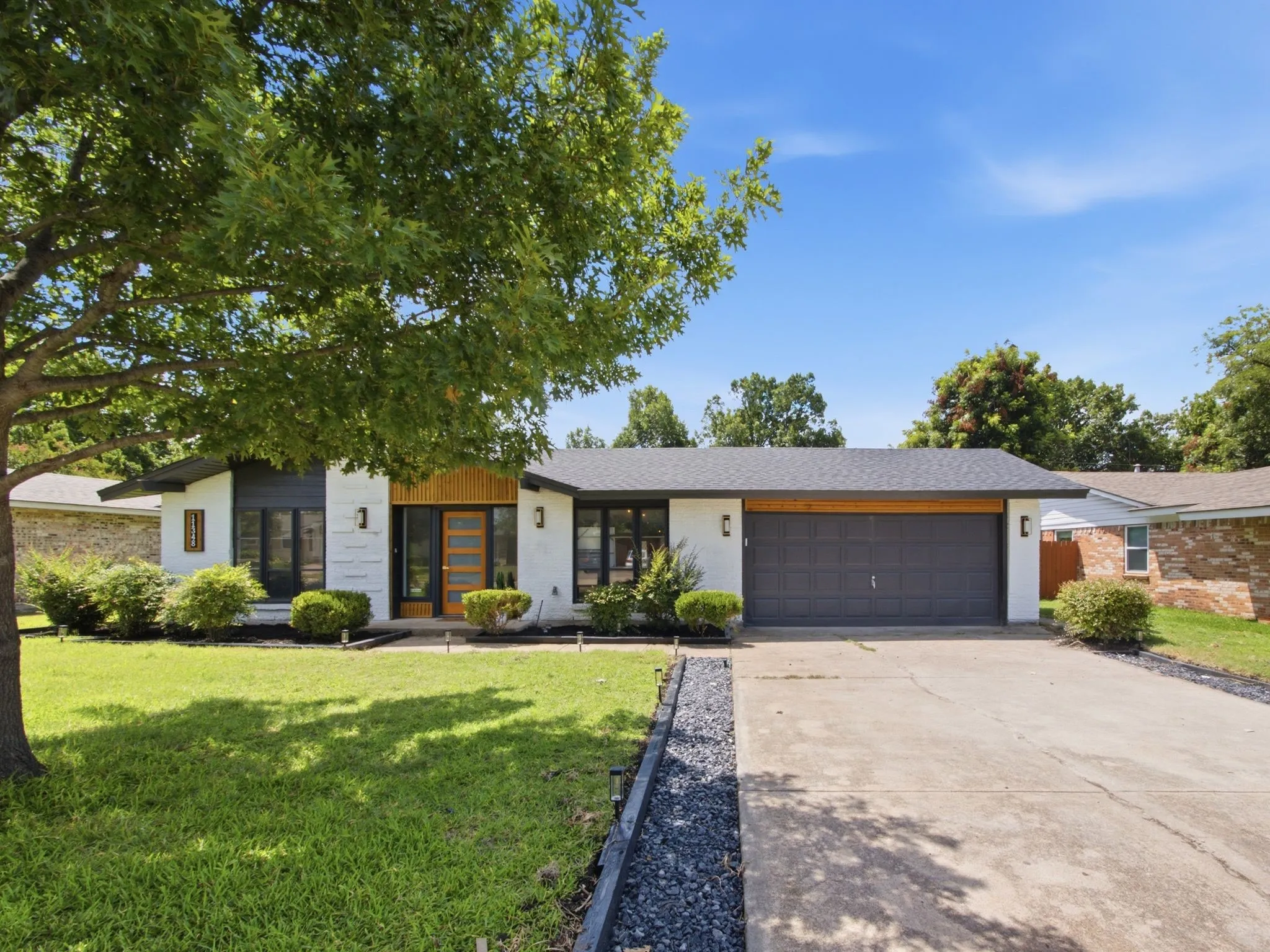 White painted brick exterior with dark trim accents, natural wood-finish front door, attached garage with a dark sectional door, and a concrete driveway