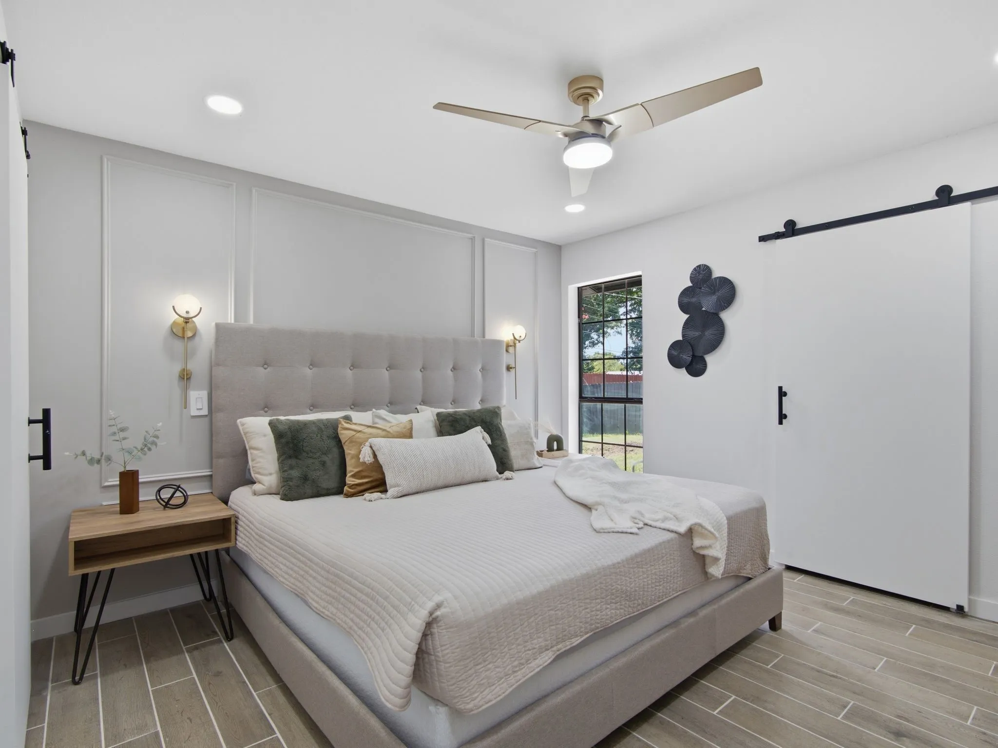 Modern primary bedroom featuring a tufted upholstered headboard, recessed and pendant lighting, ceiling fan with integrated light fixture, wood-finish flooring, and floor-to-ceiling built-in cabinetry with shaker-style doors