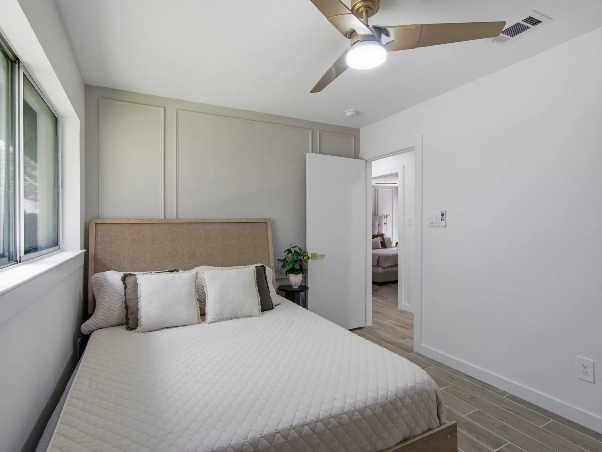 Wood-finish flooring, ceiling fan with integrated lighting, window, paneled wall accent, and white trim throughout
