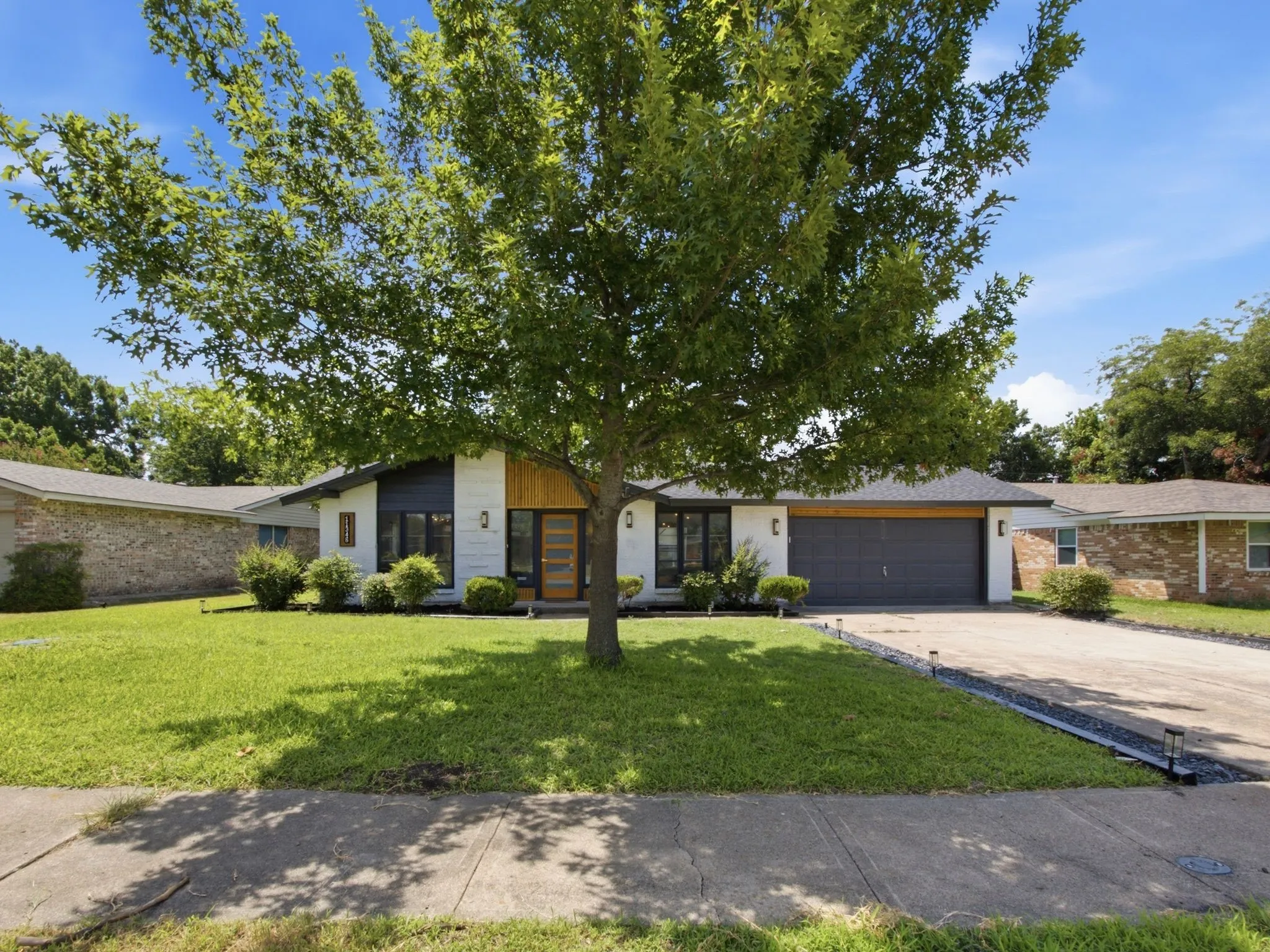 Modern facade with contrasting white and dark siding, a natural wood-tone entry, a two-car garage, and a lush green lawn