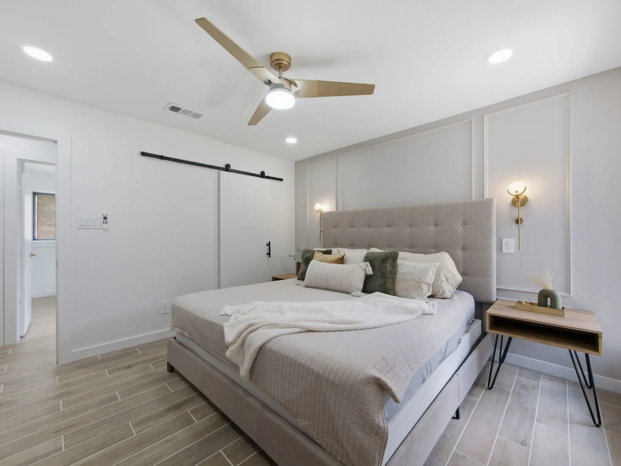 Wood-finish flooring with a plank pattern, recessed ceiling lighting, a gold-toned ceiling fan, a barn door, and decorative wall molding