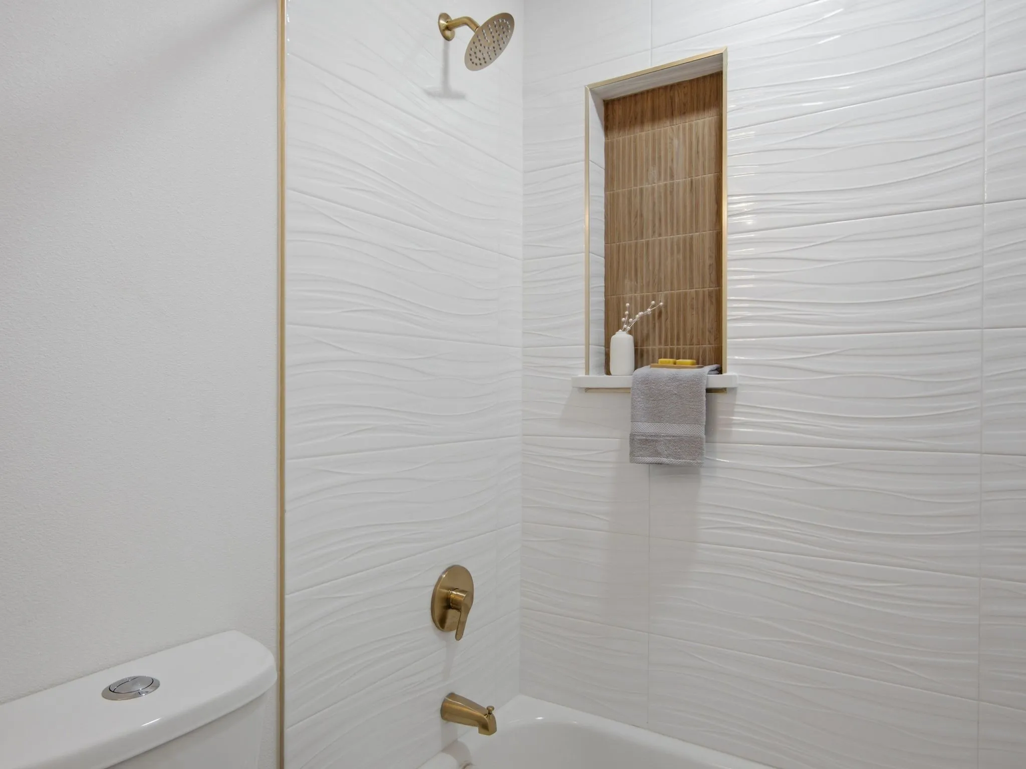 White wave-patterned wall tile, brass shower fixtures, and a recessed shower niche with wood-finish tile
