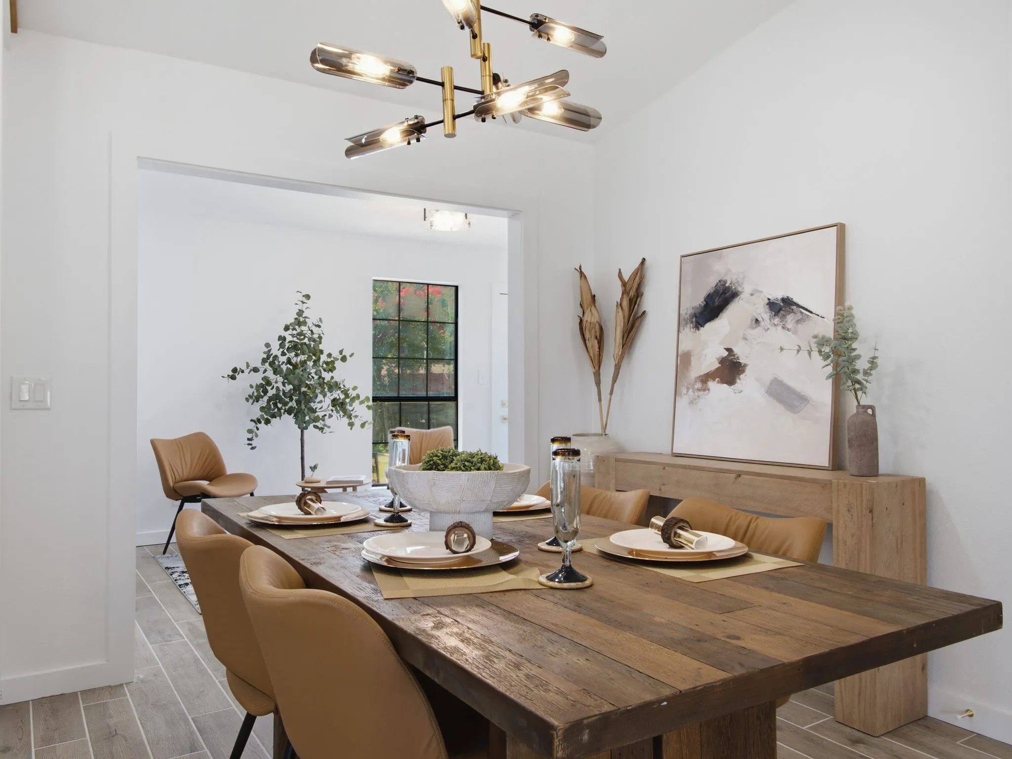 Vaulted ceiling with a contemporary chandelier, open doorway, wood-finish flooring, and a large window with grilles